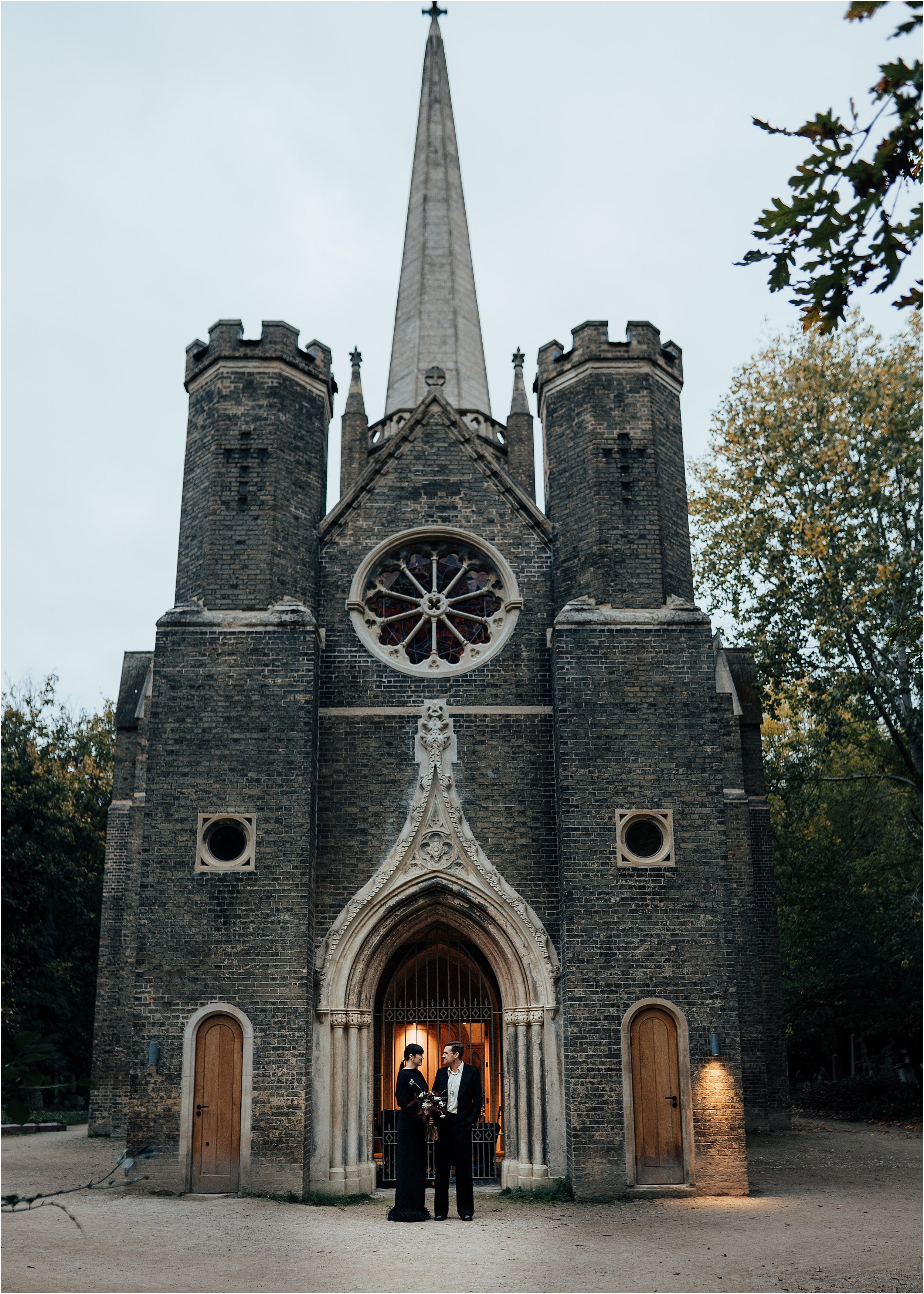 Goth bride and groom standing outside Abney Park Chapel at dusk