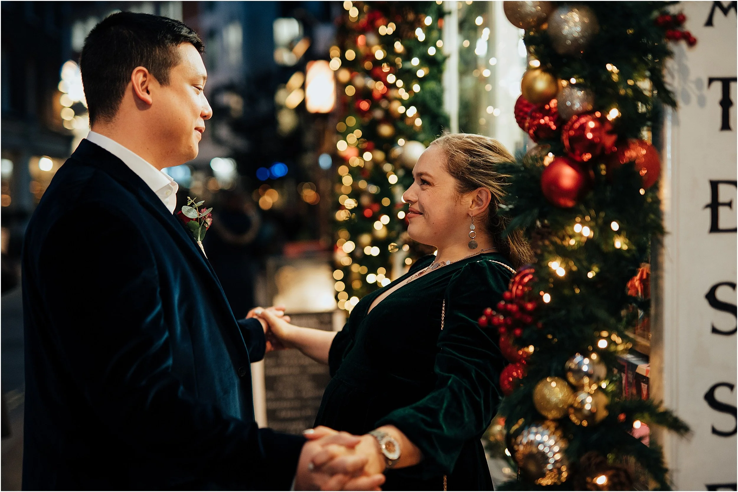 Bride and groom standing by shop with pretty Christmas lights in December