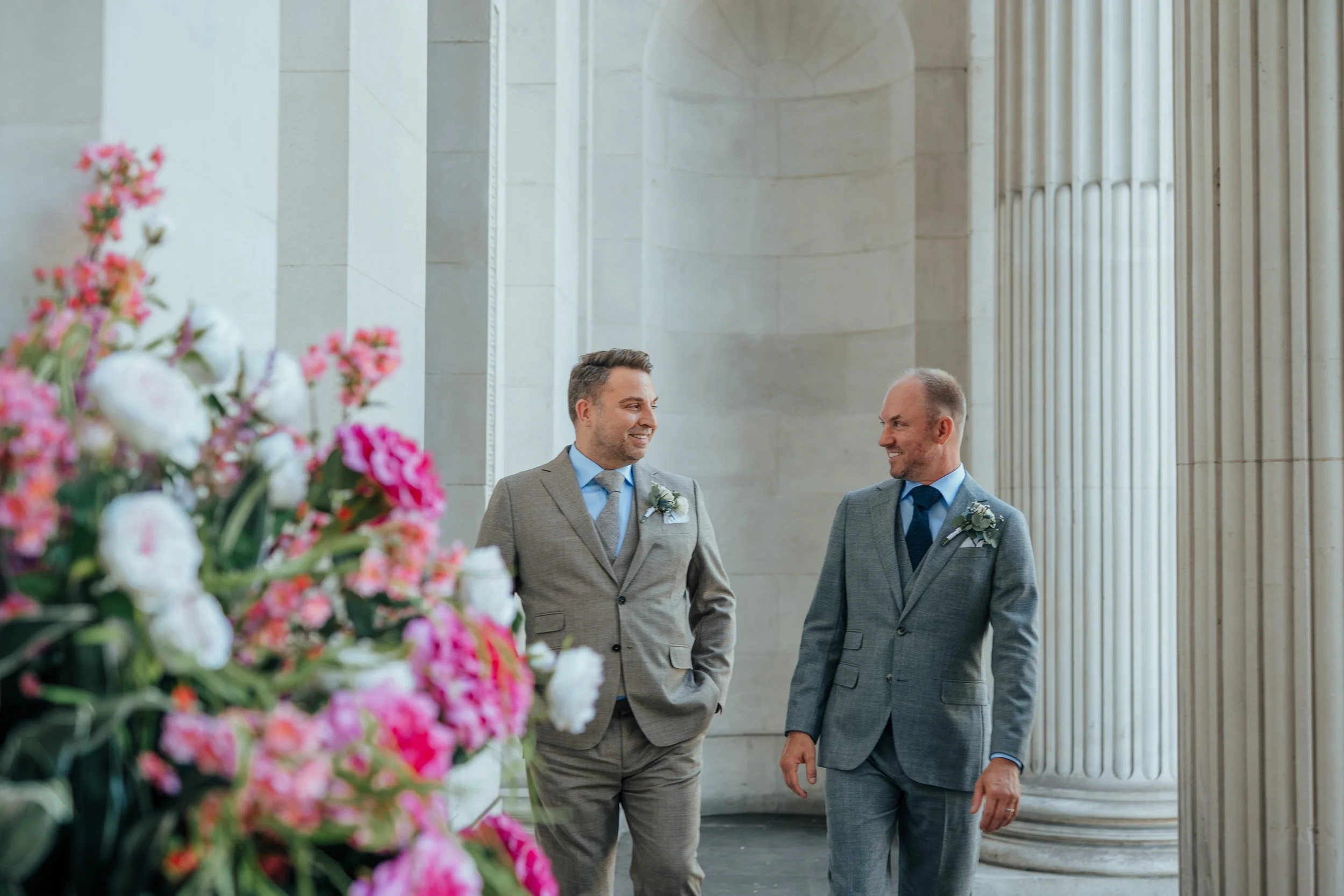 Two grooms walking along columns outside Old Marylebone Town Hall