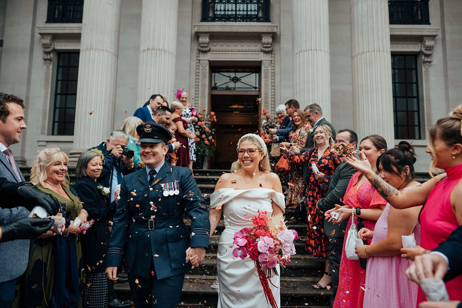 Wedding guests throwing confetti at newlyweds on steps of town hall