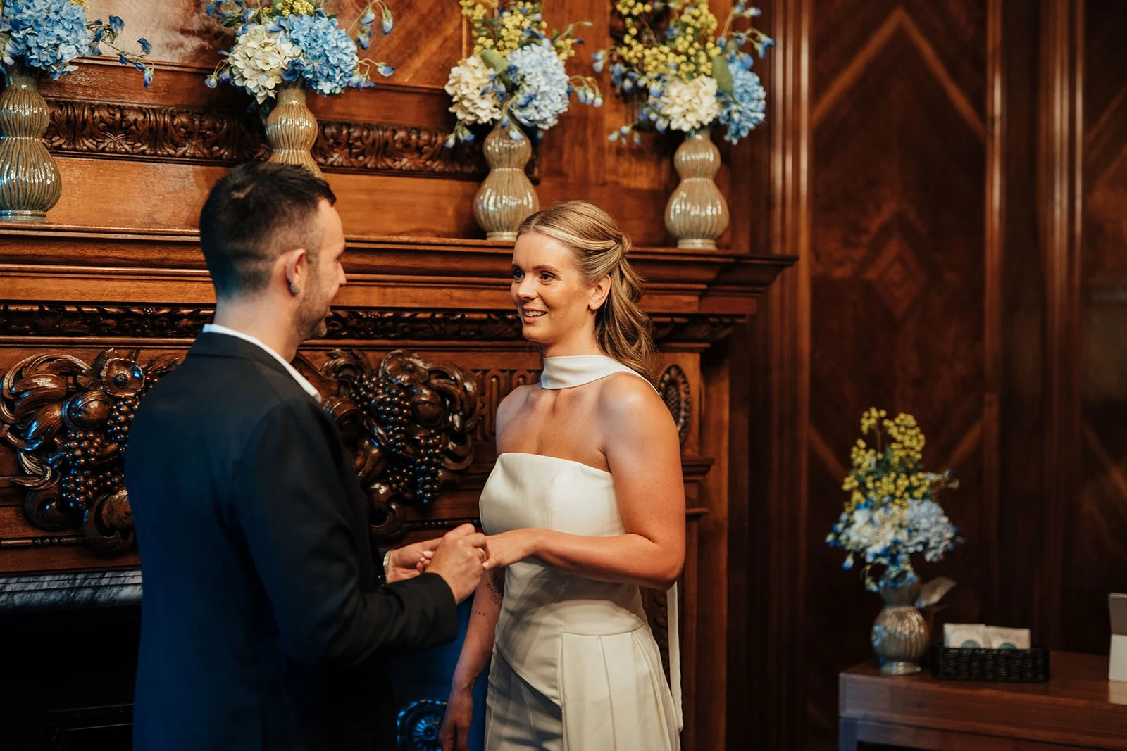 Bride and groom exchanging rings in front of fireplace in Marylebone Room