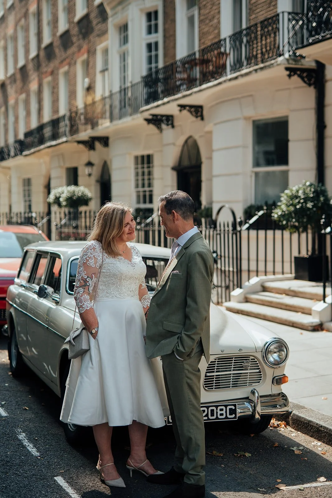 Bride and groom posing next to vintage car in Marylebone