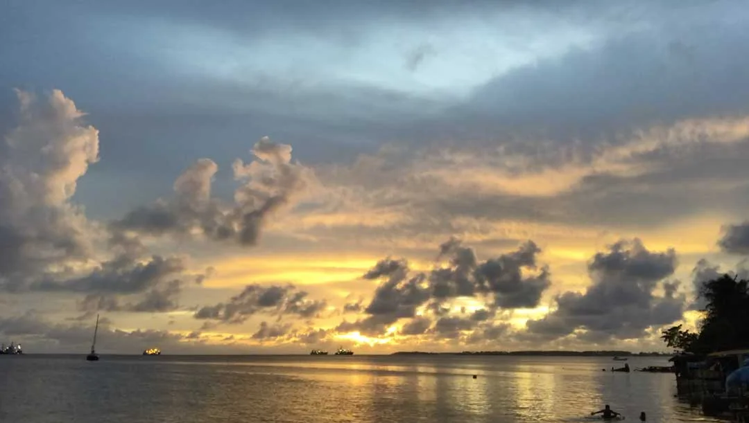 The sun sets over Majuro atoll in the Marshall Islands. Industrial fishing boats load the latest catch from the northern Pacific and children play on a makeshift styrofoam raft as the day comes to a close. By investing in early childhood development…