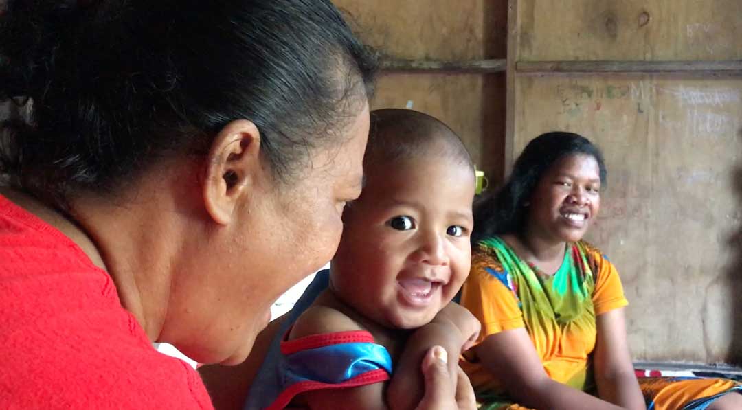 Twenty year old single mum Joanna looks on as her son plays with Jonita Alik from the home care support service for younger moms in the Marshall Islands. Women from WUTIMI go out into communities to identify vulnerable mothers and ensure they get go…
