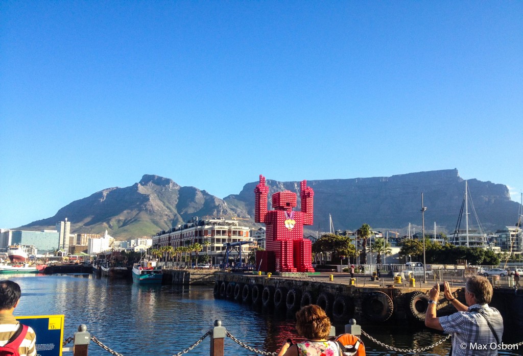 View of Table Mountain from Victoria Harbor. The giant guy is made of coke crates and has the 6 2012 Olympic medals around his neck.