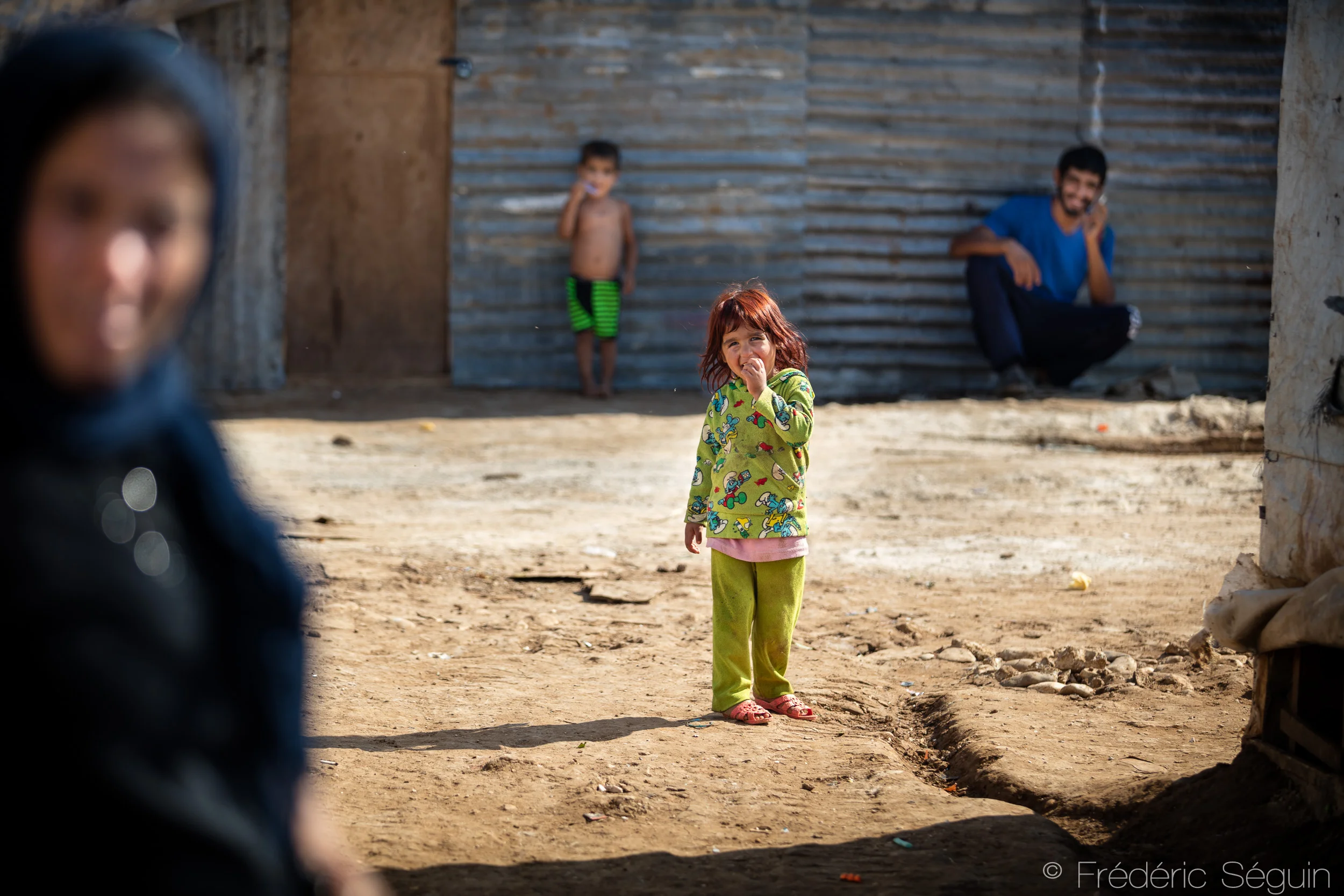 Among her relatives, a little girl smiles at the camera. Around 20 families live in the camp that has been reestablished in this location for one year. Akkar District, Lebanon. Photo credit: Frédéric Séguin, Lebanon- The Other Side of the Sea .