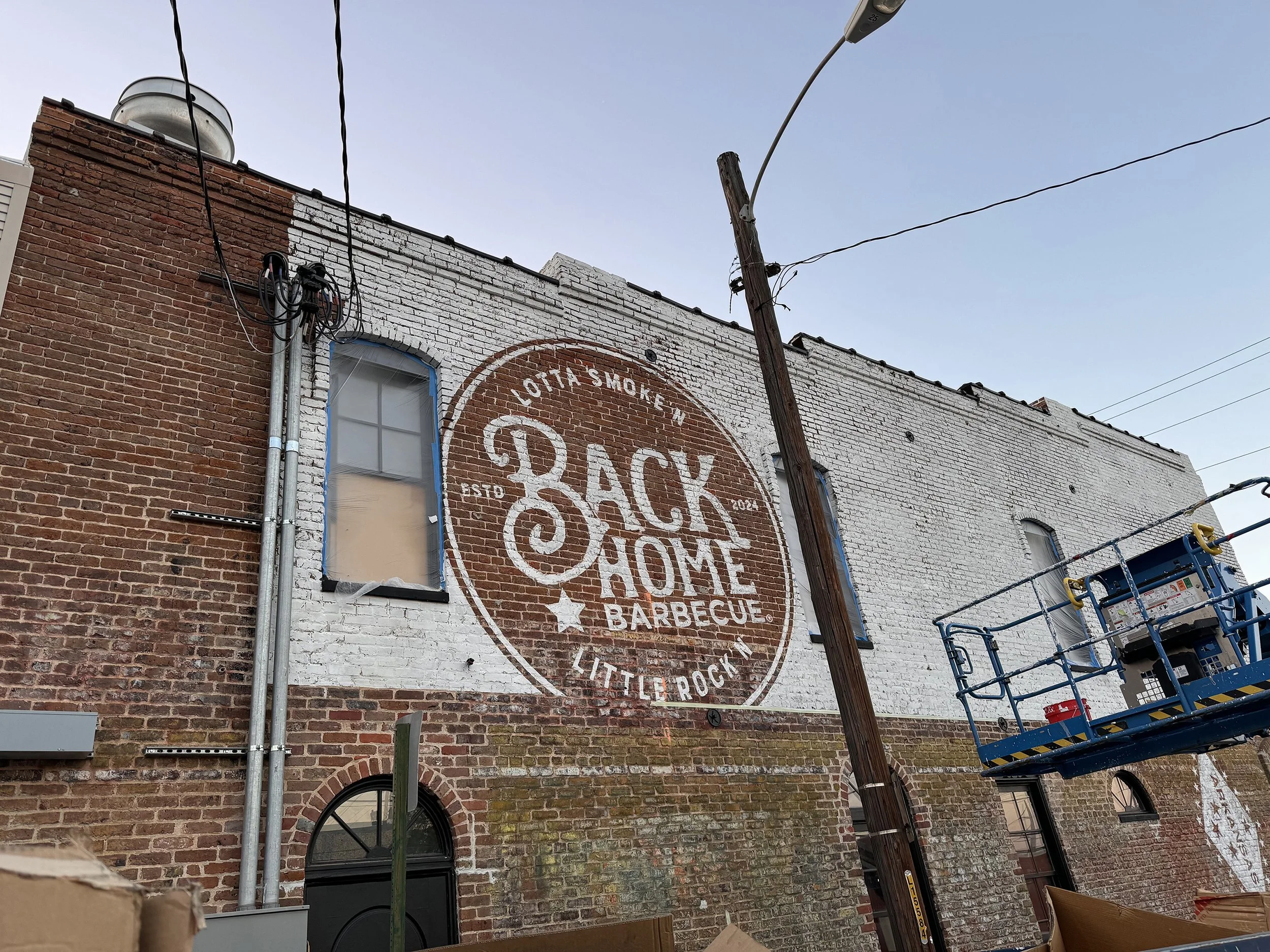  Back Home Barbecue  Little Rock, Arkansas  East face mural in progress with tag line “LOTTA SMOKE’N - LITTLE ROCK’N” written by Chuck Mitchell  Mural design creative by Chuck Mitchell and Reid Mitchell  Mural painted by Quantavious “Toonky” Worship 