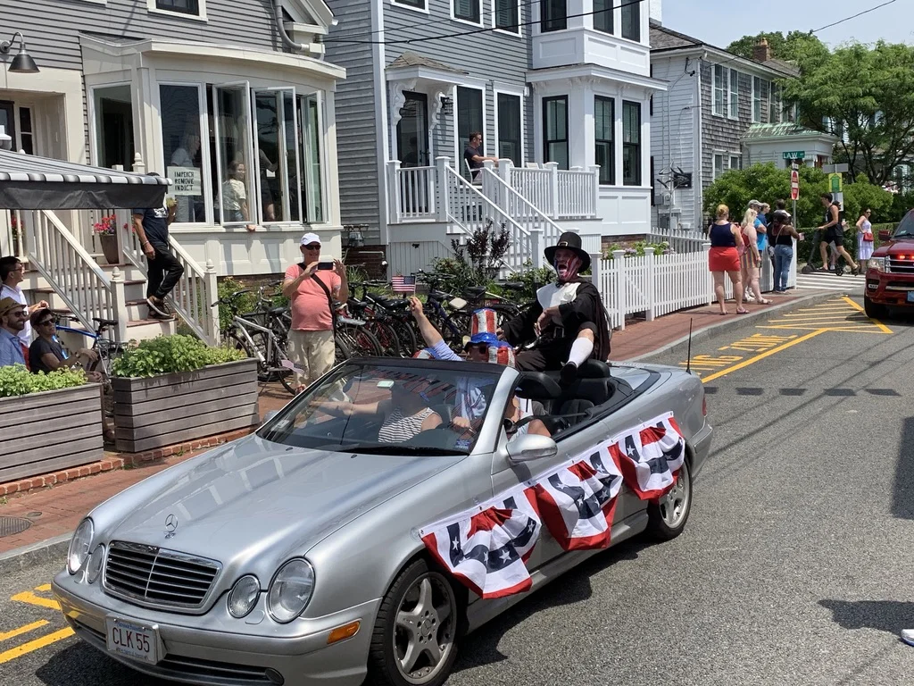 The Town Crier during the July Fourth parade, still singing “Grand Old Flag.” Note the sign in the window at left.