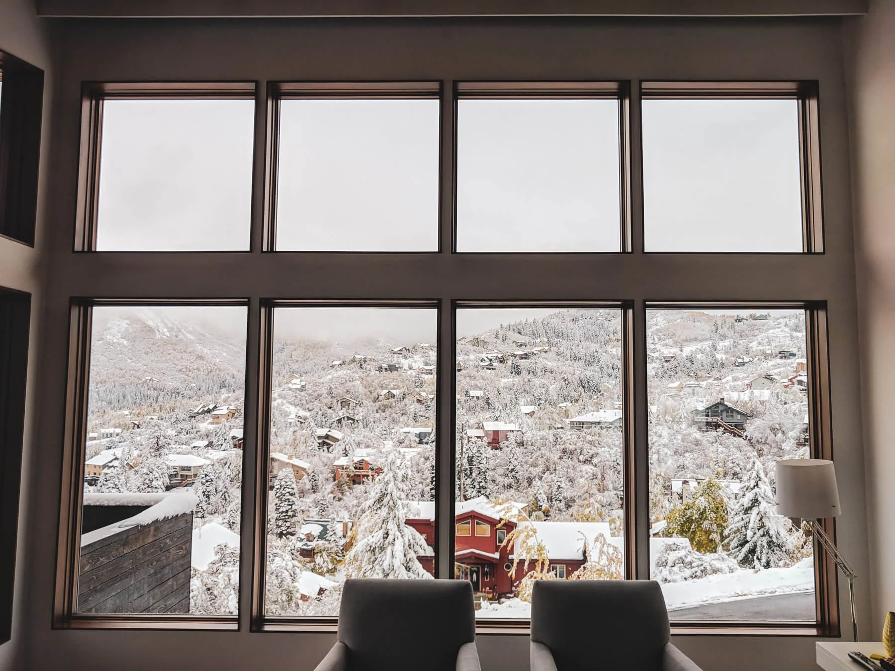 Interior view of a room with large floor-to-ceiling windows showing a snowy mountain village landscape outside.