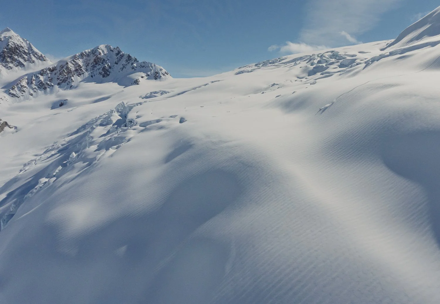 Snow-covered mountain slope with footprints trailing across fresh powder under a partly cloudy sky.