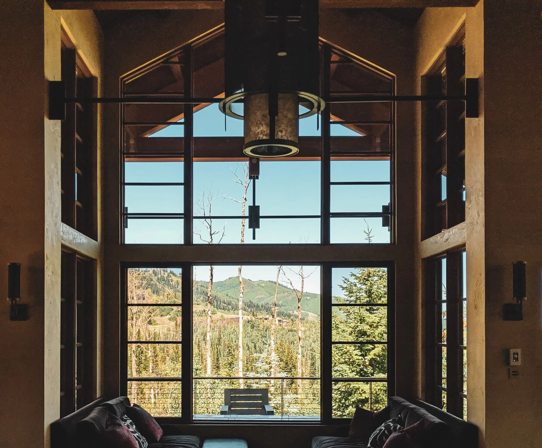 Rustic mountain home with a shingled roof, stone chimney, and large windows under a bright blue sky.