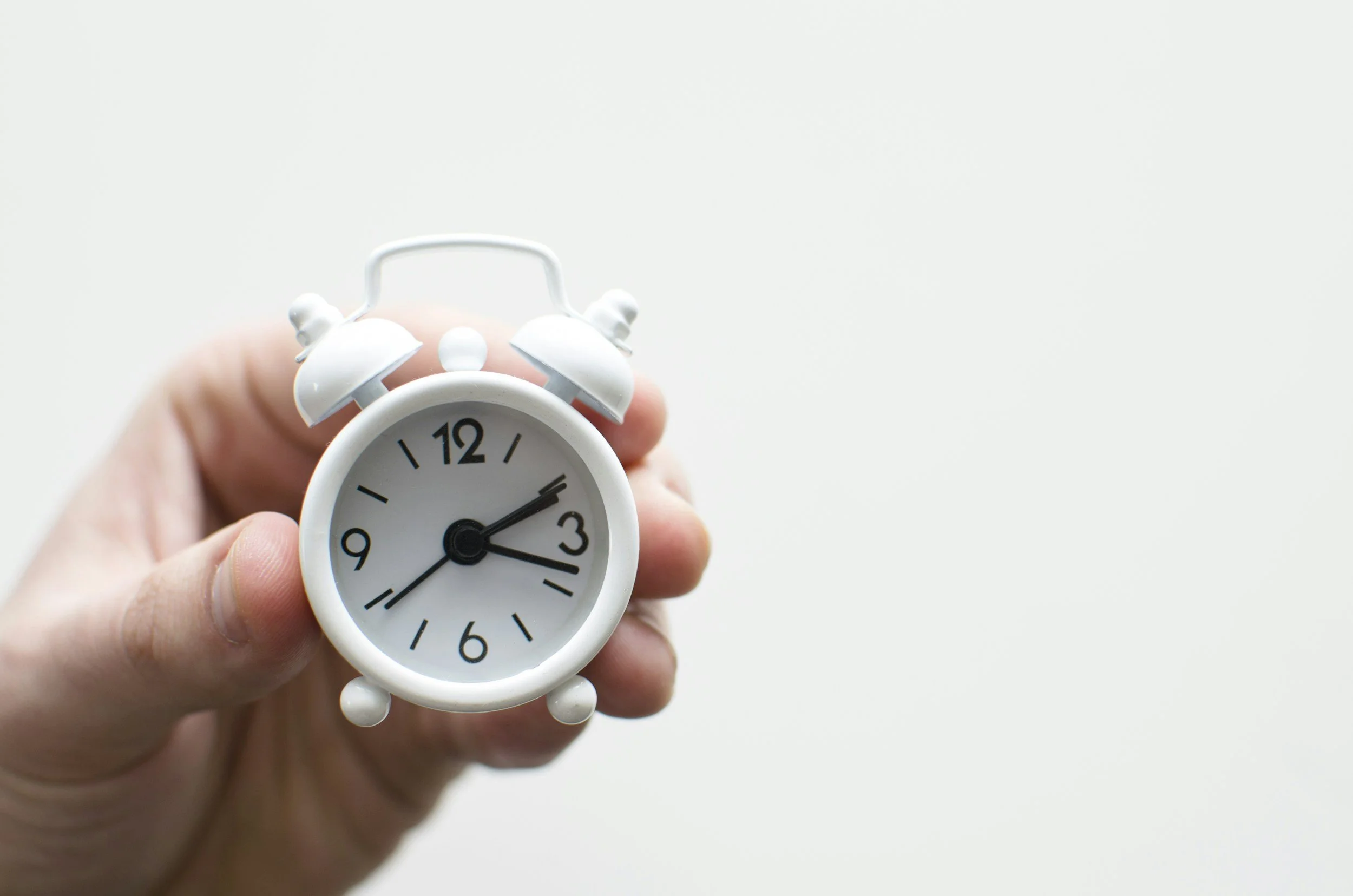 a hand holds a small white clock