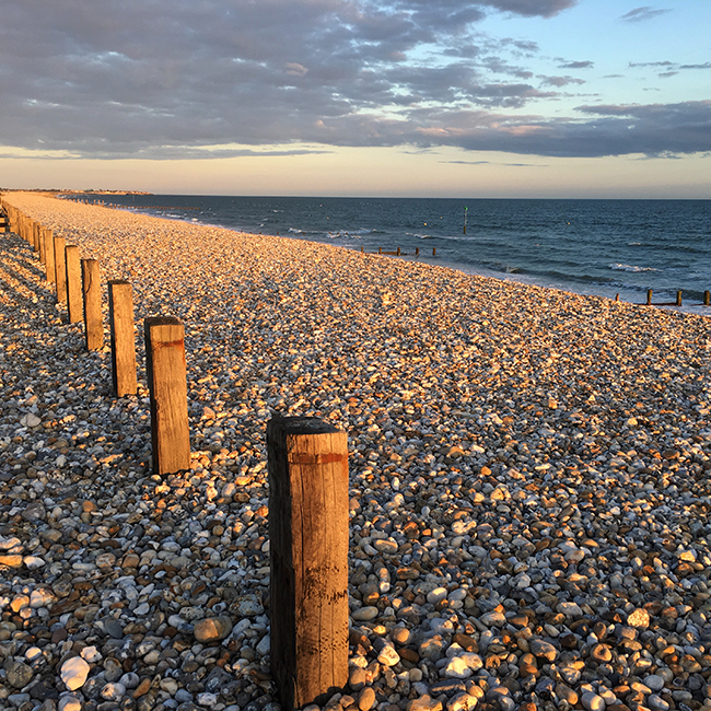 The monotonous texture of the pebbles is balanced by the wooden posts, the sea and the sky.