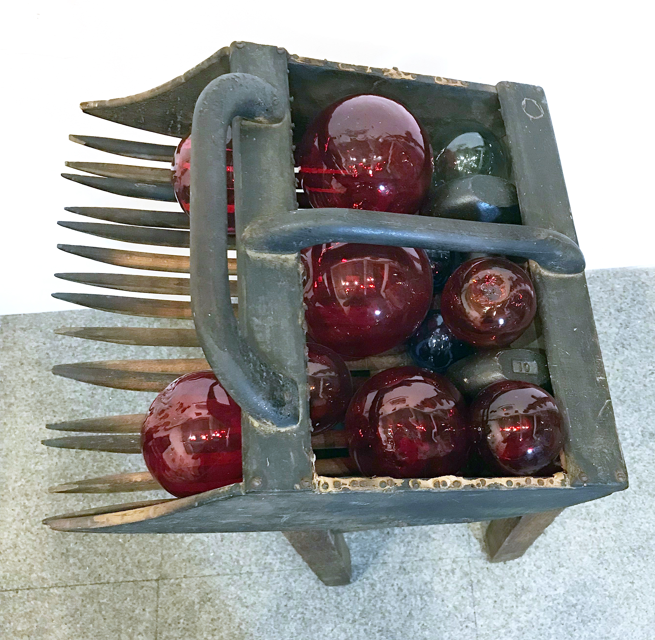 Cranberry. Assemblage of an antique cranberry rake filled with glass balls standing on an antique oak plant stand. Rake: 18x5x9"H. Stand: 12x12x25"H. Top View. 2018.