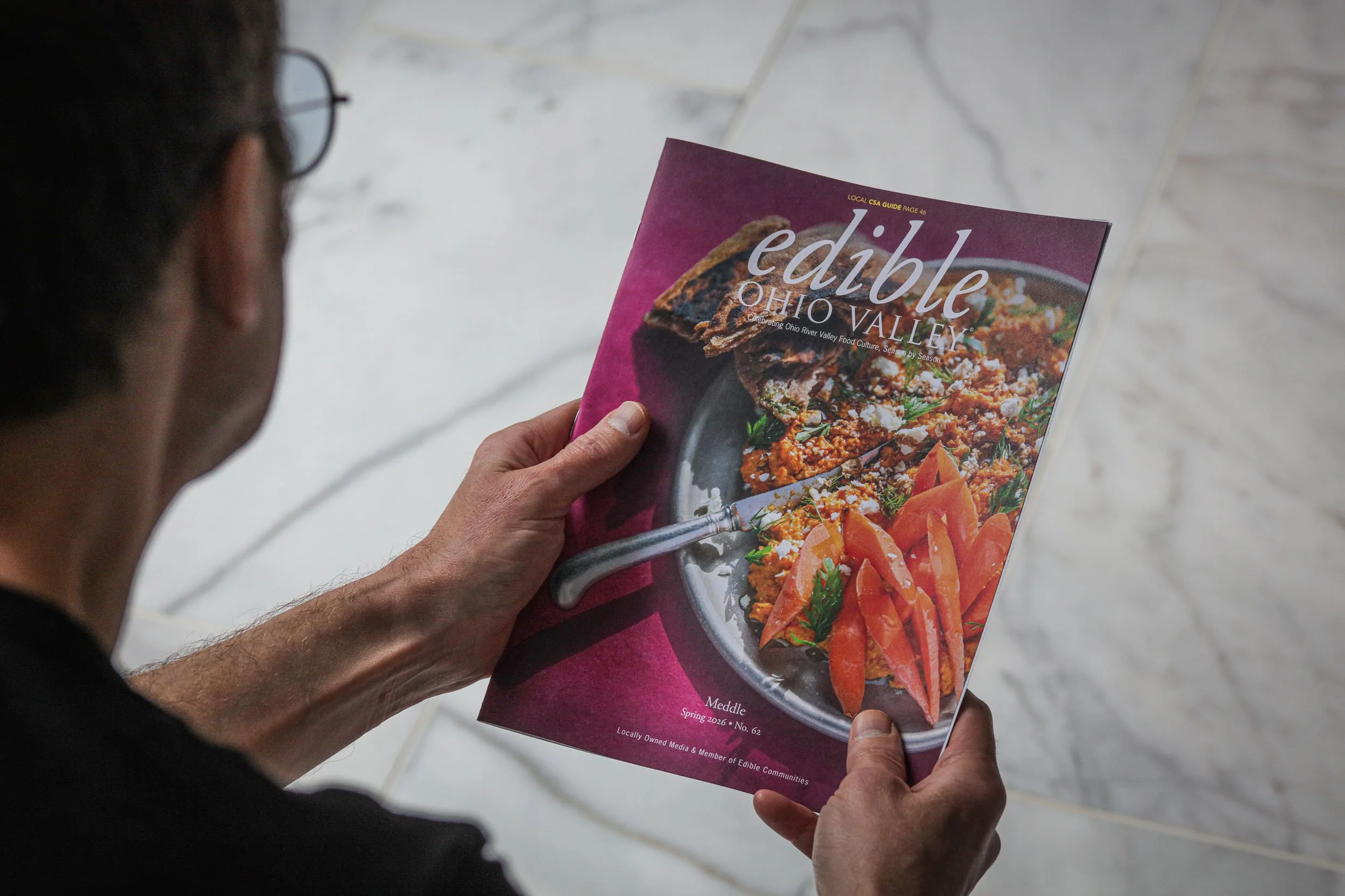 Person holding a magazine titled 'Edible Ohio Valley' with a cover photo of a plate of healthy food.