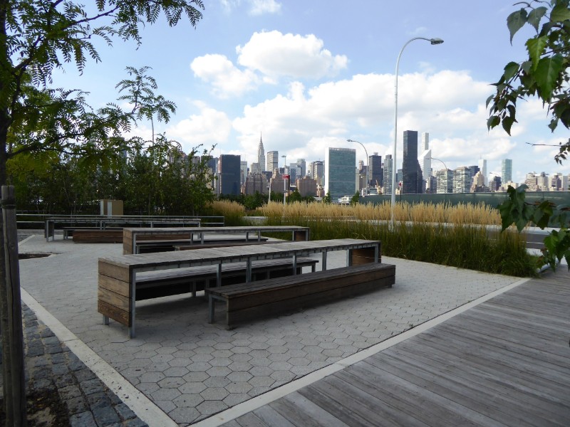 Picnic area along walkway from urban development to waterfront park with Manhattan on skyline
