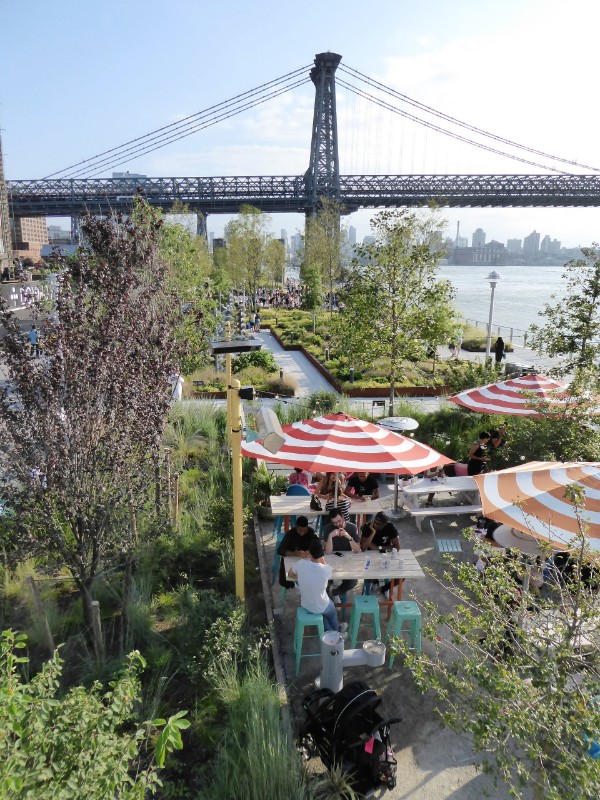 View over park  from elevated walkway with outdoor eating area &amp; Williamsburg Bridge beyond