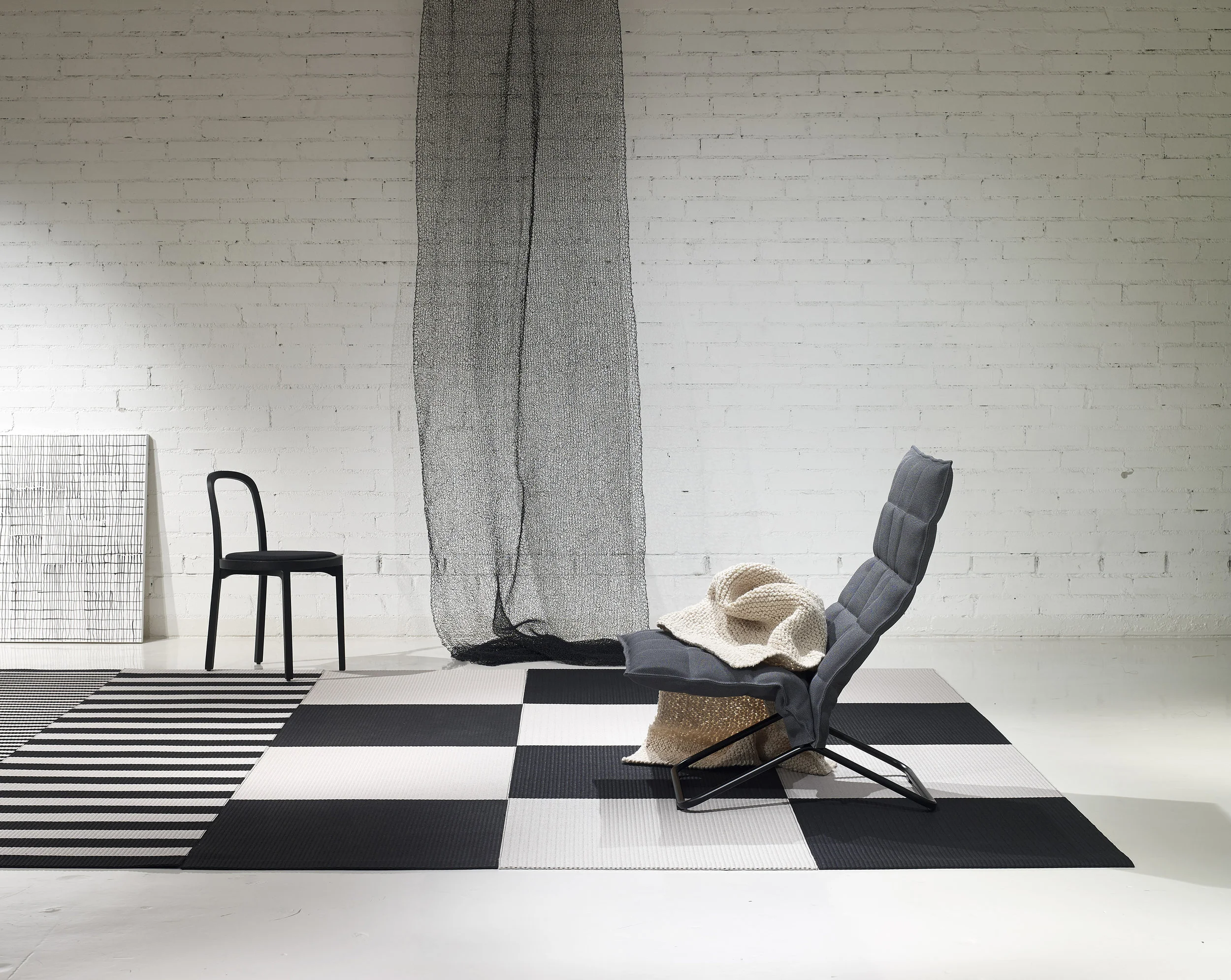 Woodnotes interior / Squareplay paper yarn combo with 1420915 Big Stripe and 1190915 Stripe paper yarns black-stone, 46003 Narrow Tubular k Chair col. graphite matt-black tubular frame, 4419 Siro+ black seat leather upholstered, 7300101 Woodwool hand knitted throw col. white and 7110902 Mesh hand knitted partition black-steel.