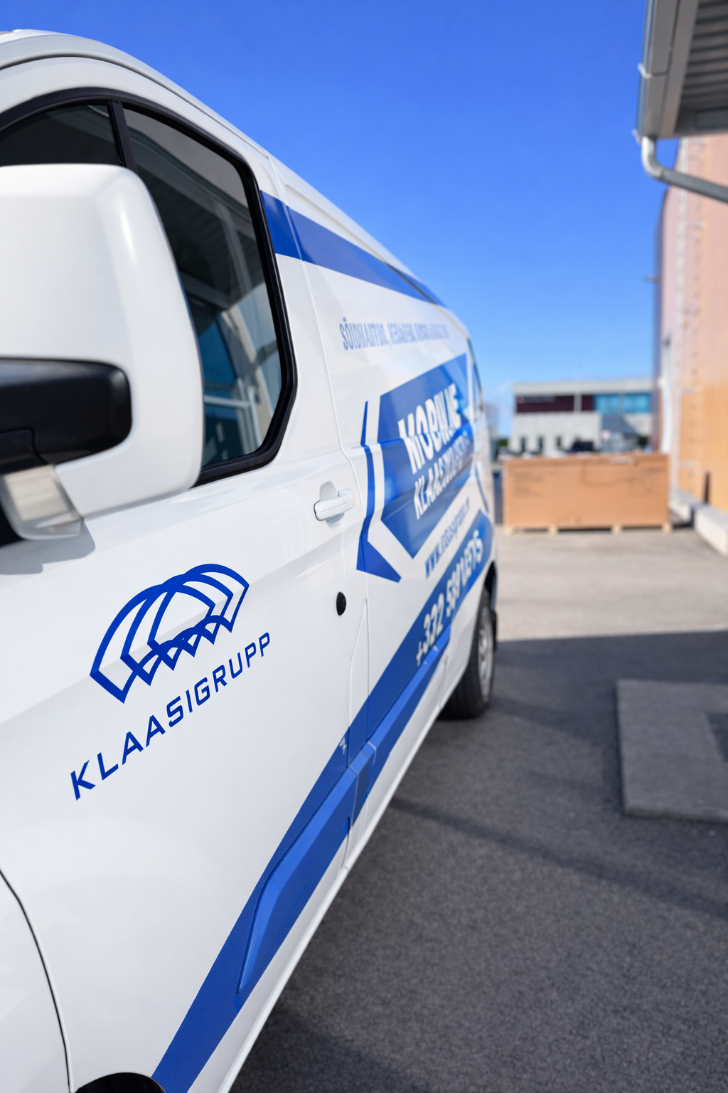 A white van with blue branding and text parked outside a building on a sunny day.