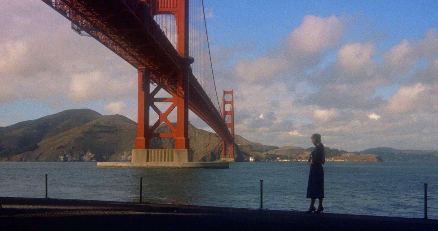 A woman stands alone in front of the Golden Gate Bay with the Golden Gate Bridge and Marin hills behind her.