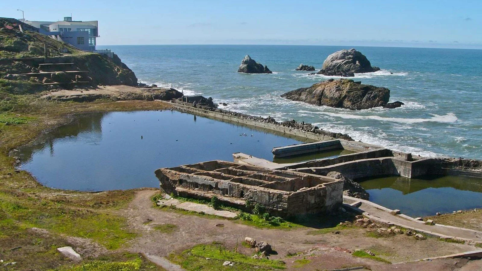 Several large pools of water in-between some ruins of what once used to be a bathhouse overlook the ocean.