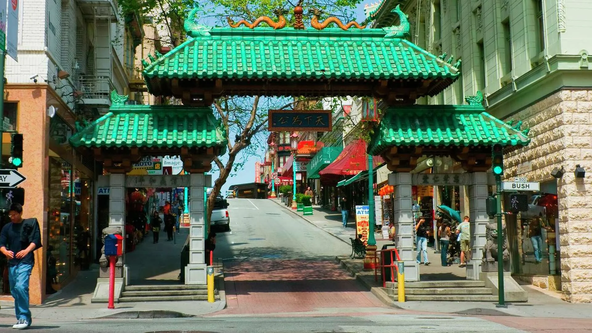 A green Chinese style gate spans a street. There are orange Asian dragons facing each other on top of the middle of the gate.