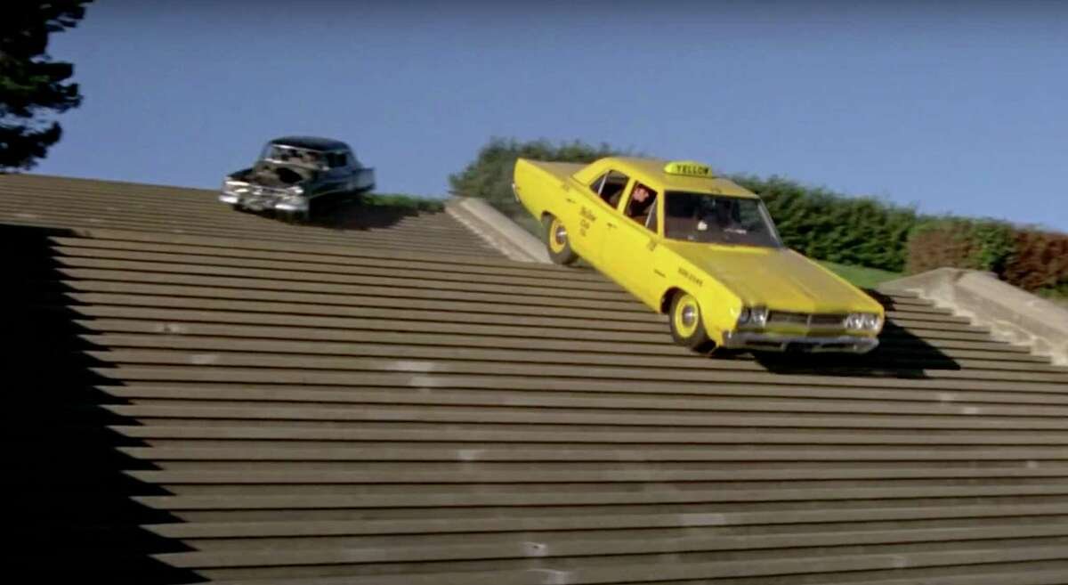 A bright yellow taxi and black car drive down a steep staircase.