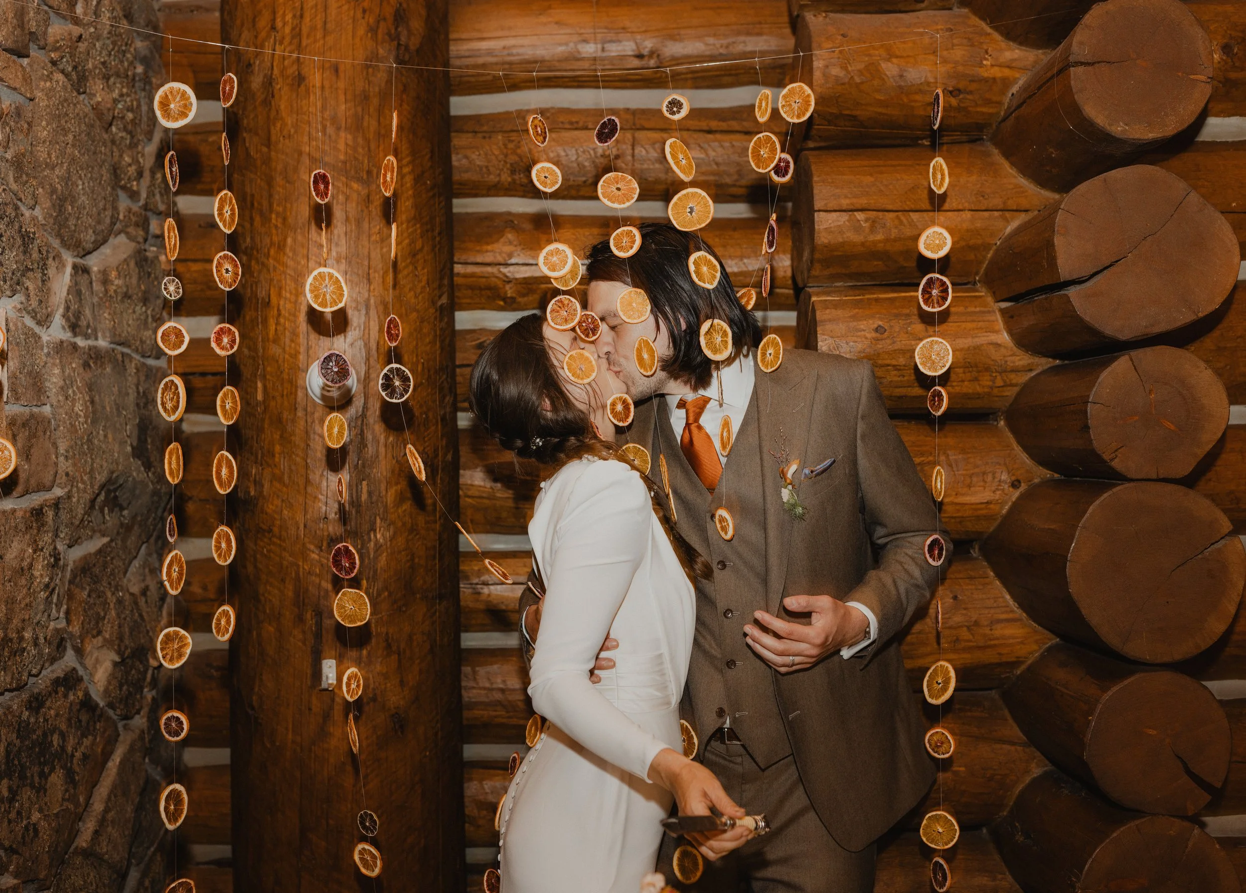 A couple sharing a kiss in a rustic wooden setting decorated with hanging dried orange slices.