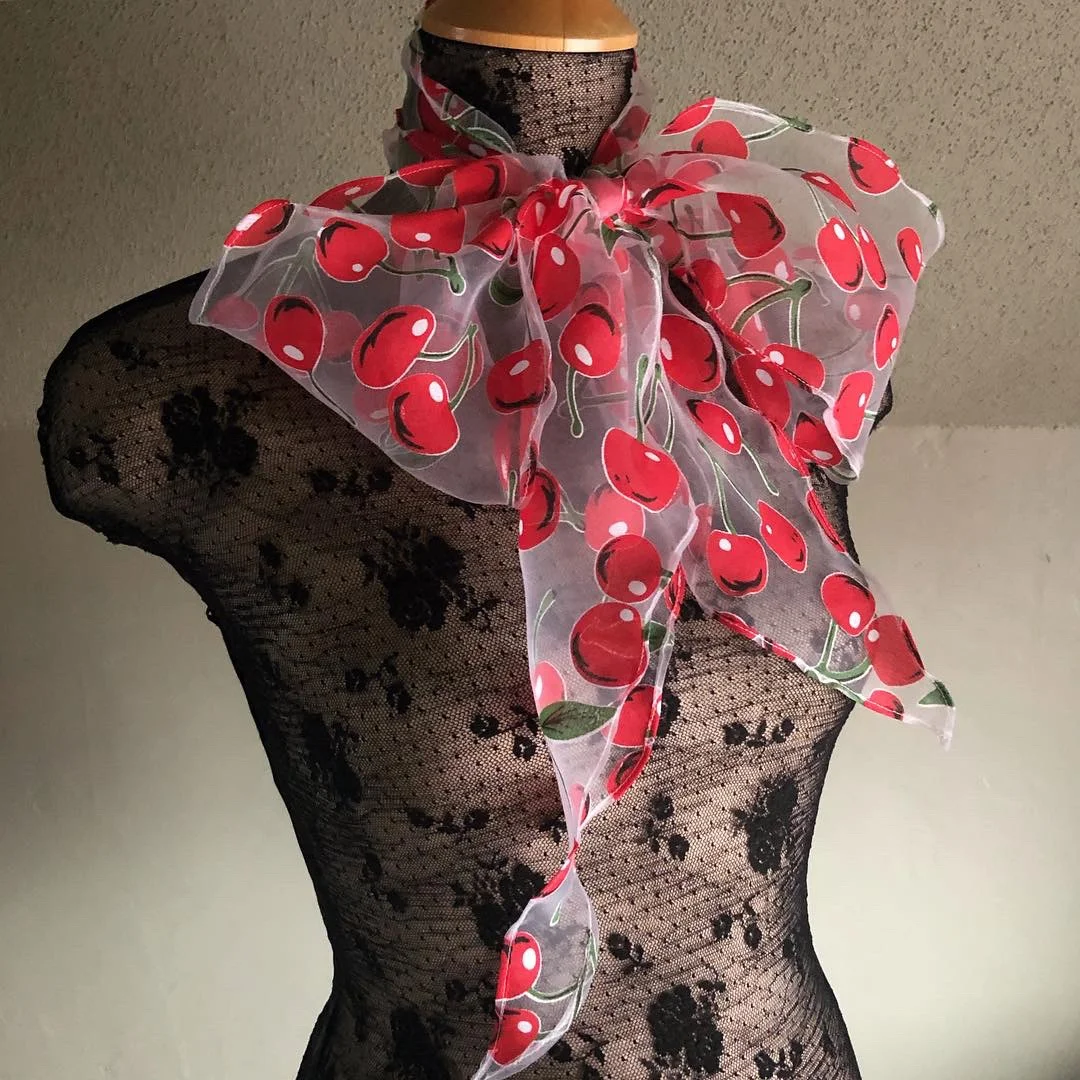 Side view of a giant bow scarf in sheer white organza printed with red cherries