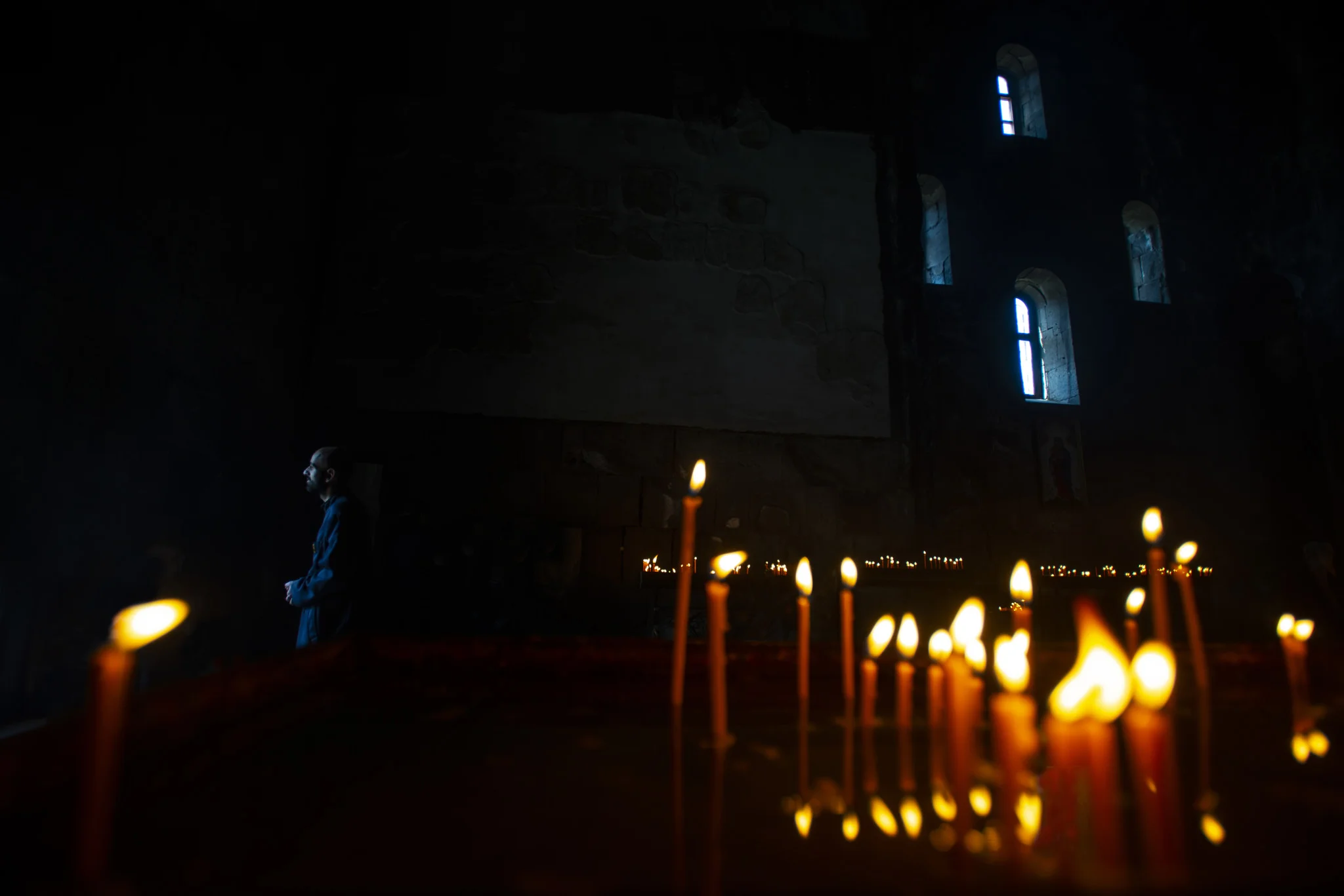 a priest in a church with candles, tatev, armenia.jpg