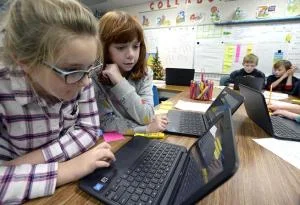Celia Davis, 9, left, and Aidan Coble, 9, center, Carrie Martin Elementary School fourth-graders, check out their stock on a computer during gifted and talented class Thursday, Dec. 6, 2018, at the school in Loveland. During a unit on the stock market, the students learned how to research and trade stocks as a virtual lesson. Three kids in the class won first and second place against students across the state by earning the most growth in their portfolios. Aidan is one of the students who won second place. ( Jenny Sparks / Loveland Reporter-Herald )