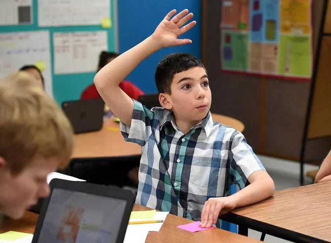 Carrie Martin Elementary School Bradyn Cronin, 10, raises his hand to answer a question about the stock market during gifted and talented class Thursday, Dec. 6, 2018, at the school in Loveland. During a unit on the stock market, the students learned how to research and trade stocks as a virtual lesson. Three kids in the class won first and second place against students across the state by earning the most growth in their portfolios. Bradyn is one of the students who won first place ( Jenny Sparks / Loveland Reporter-Herald )