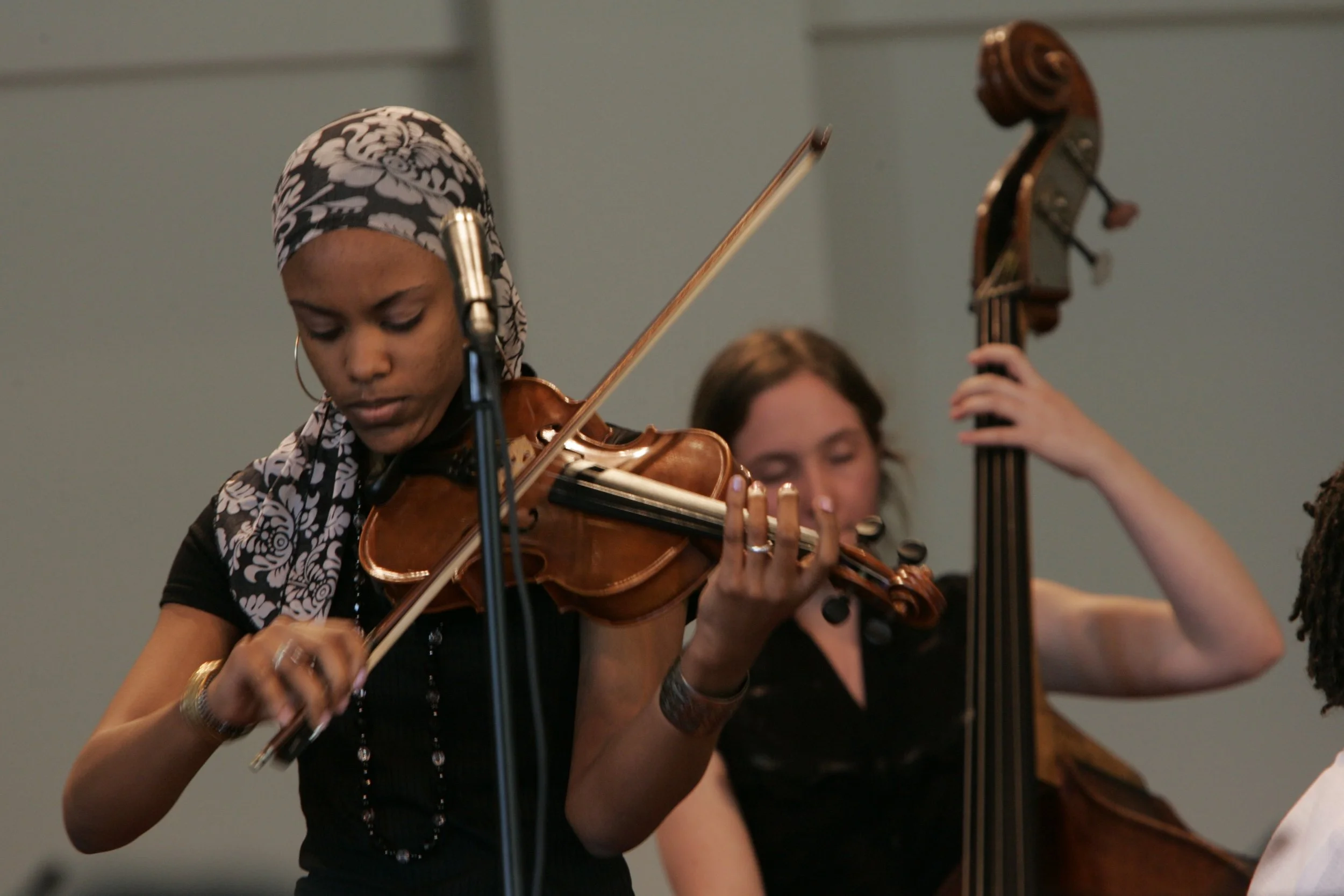 Woman playing violin in front of another person playing bass.