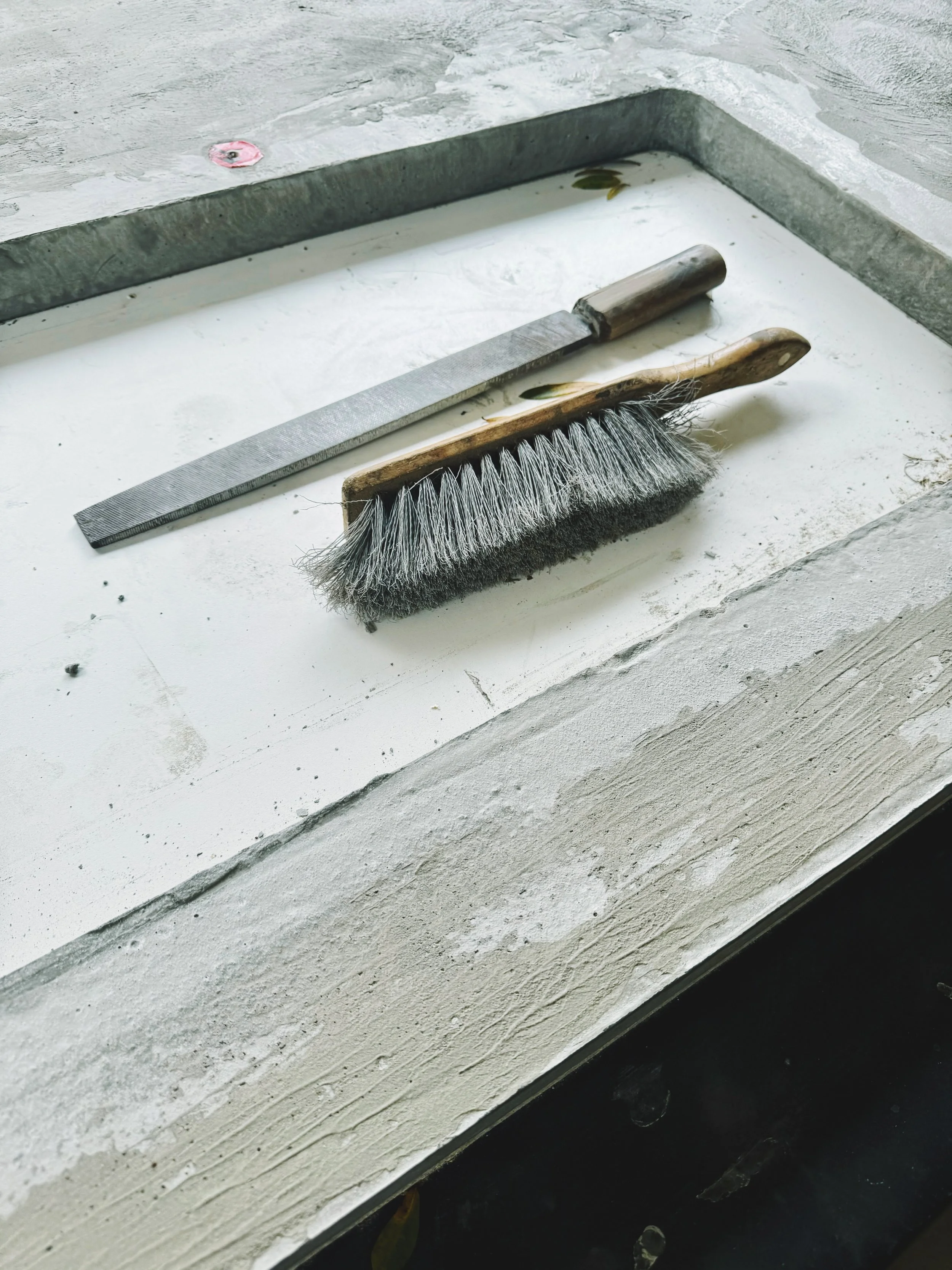 Cleaning tools on a windowsill, including a metal file and a scrubbing brush with a wooden handle.