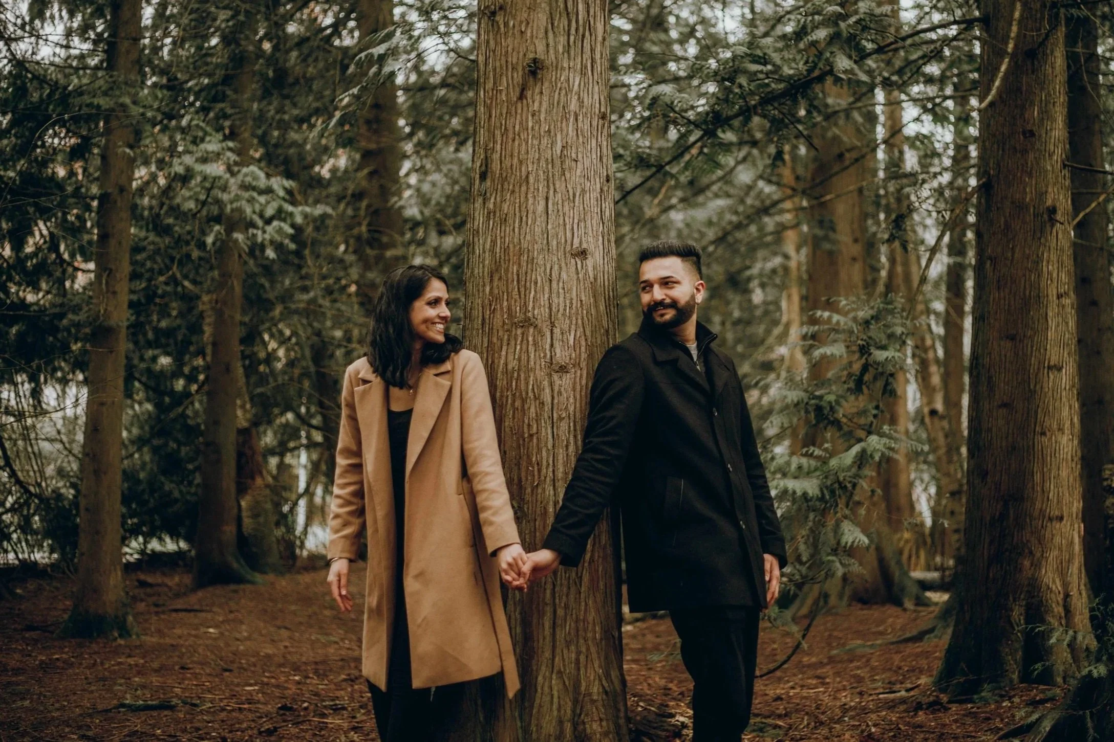 Vancouver couple takes shelter from the rain under a canopy of evergreen trees, the best trick for when it rains on the day of your photo session in BC.