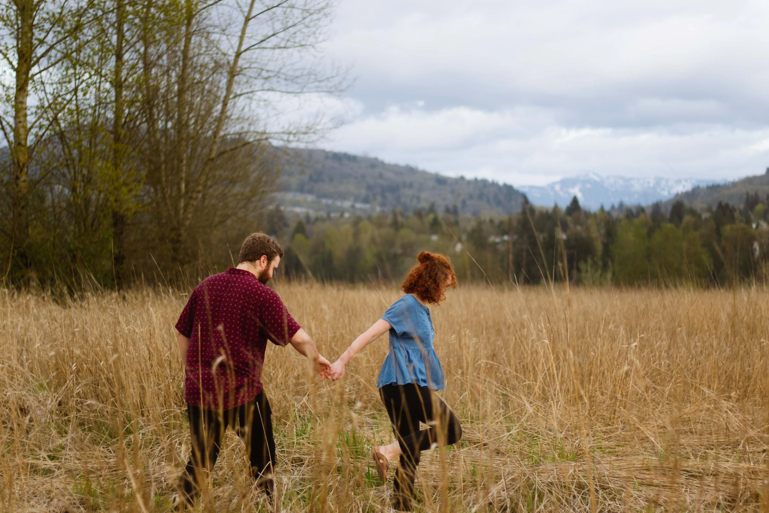 Vancouver couple holds ands and walks through tall grass at Willband Creek Park