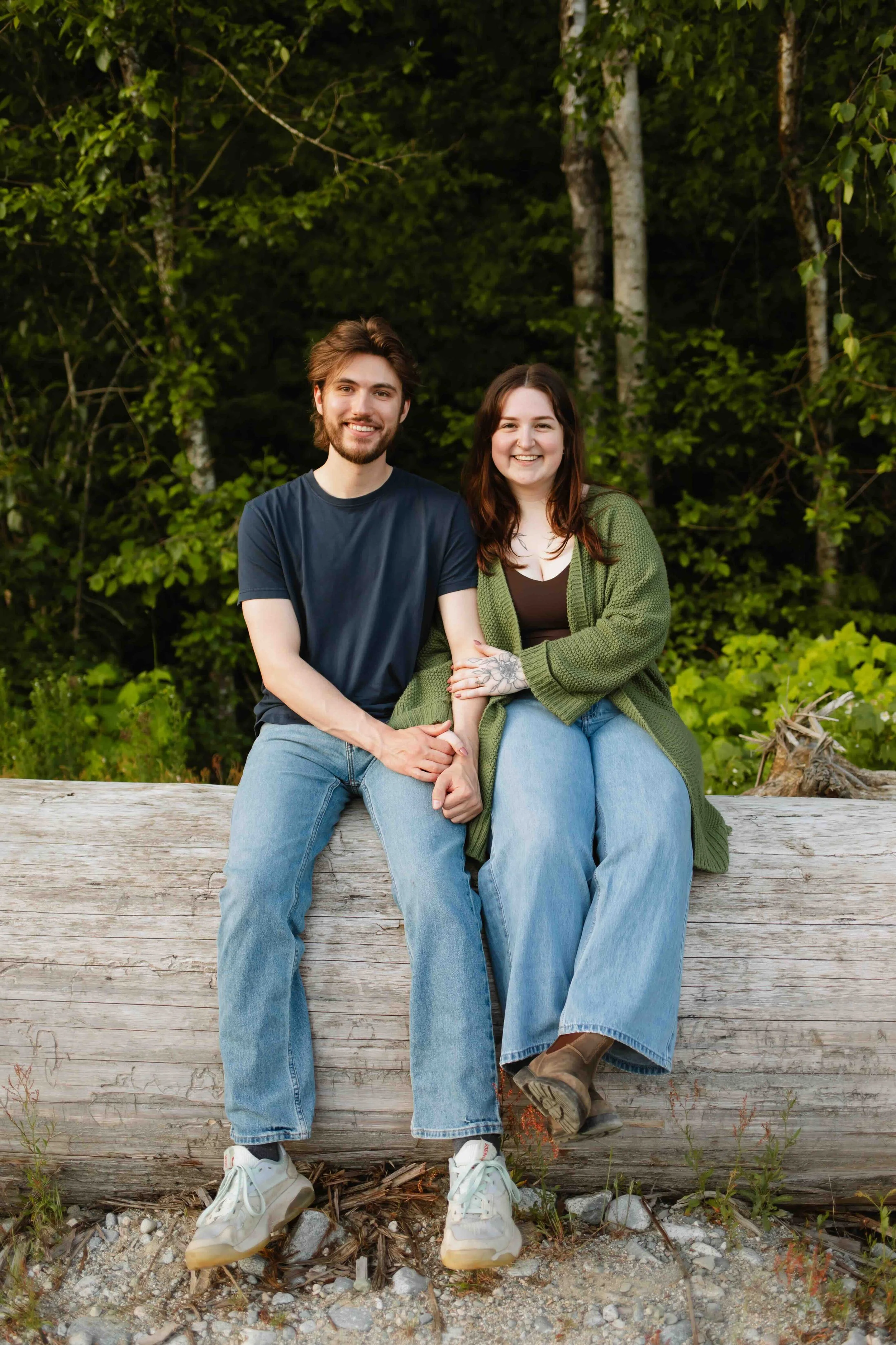 Vancouver couple sits on a log with arms intertwined, smiling at the camera