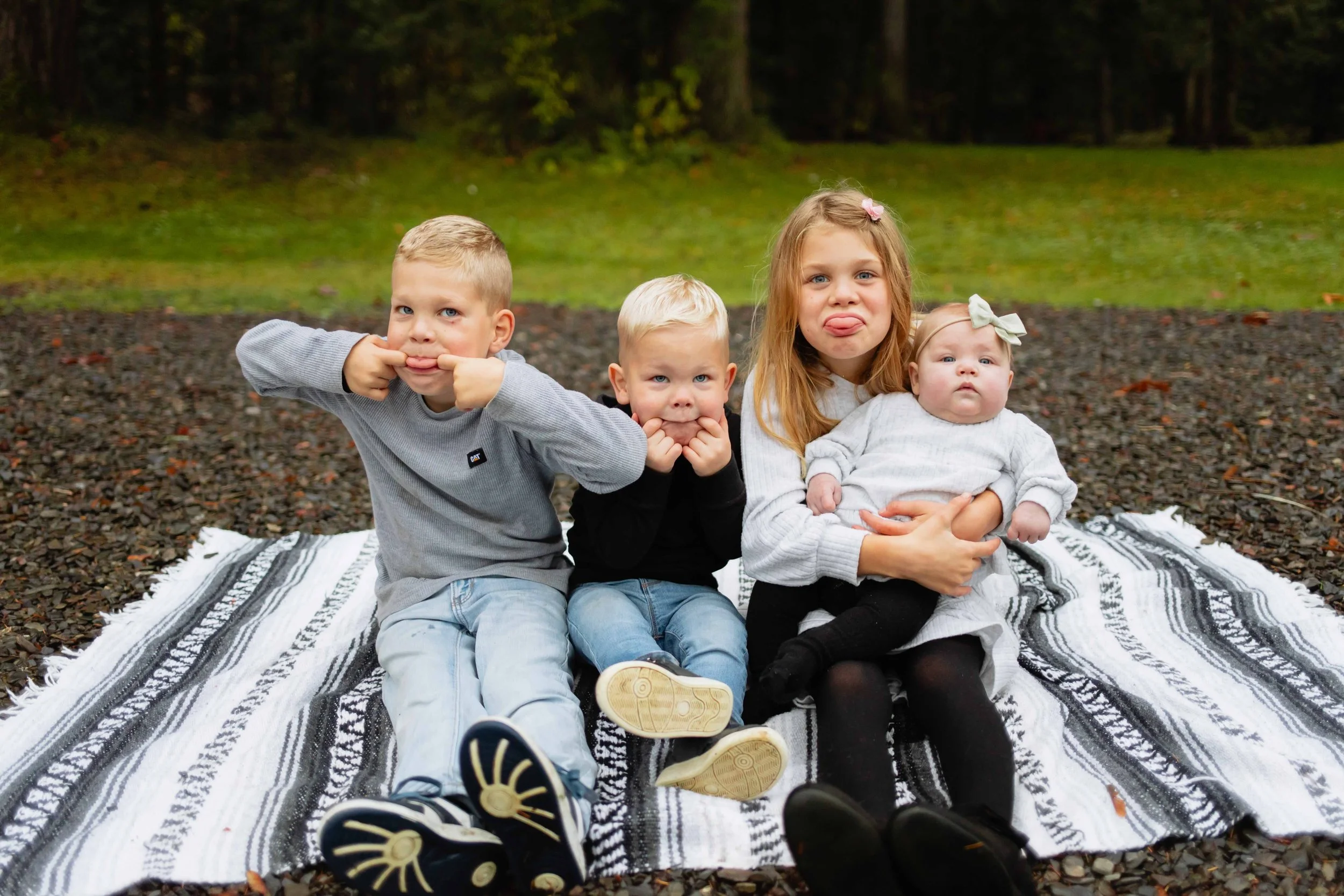 Young Vancouver children make fun and silly faces at camera holding newborn baby