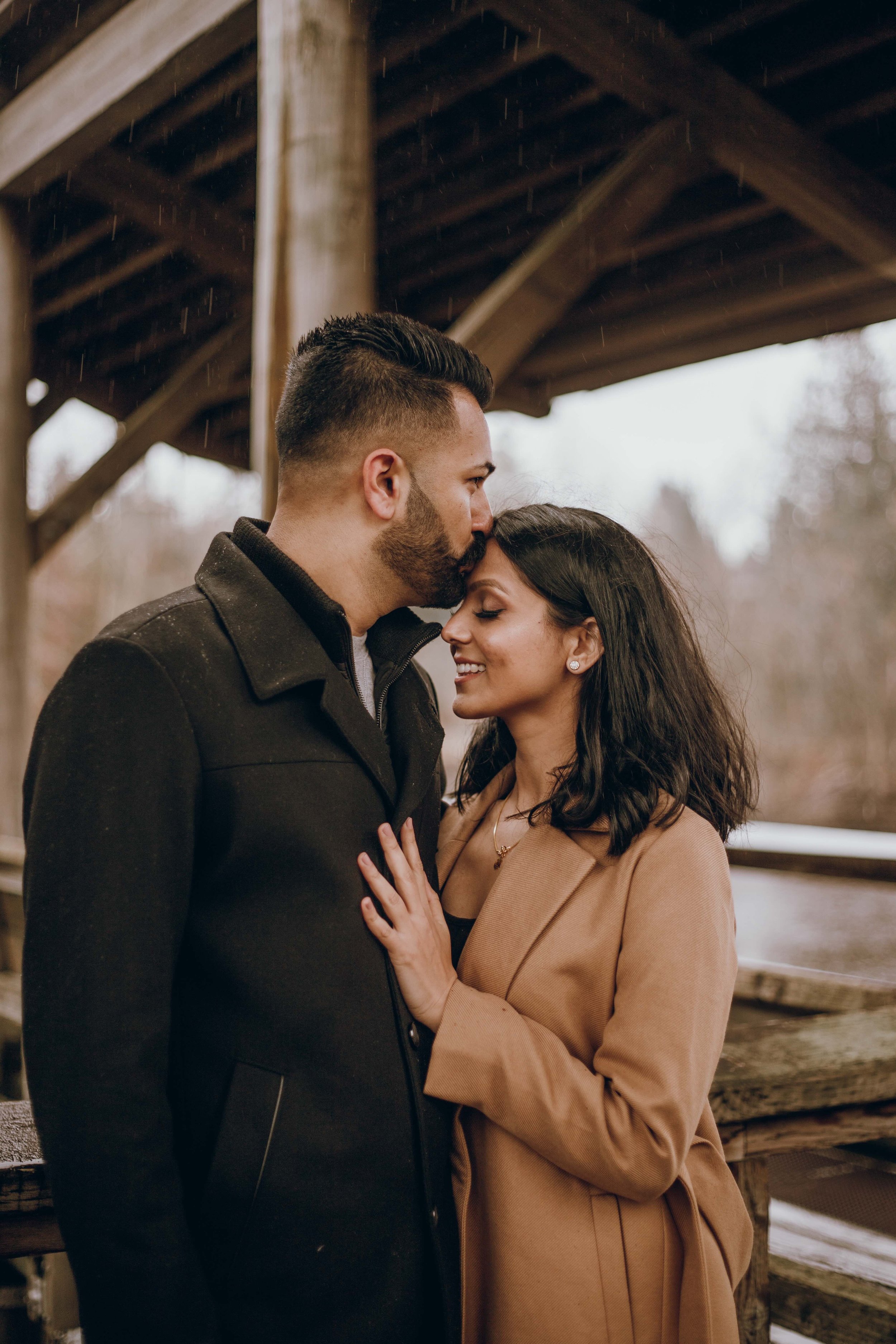 Vancouver couple snuggles under wooden gazebo at Fishtrap Creek Park, the best location for rainy day photos in Abbotsford.