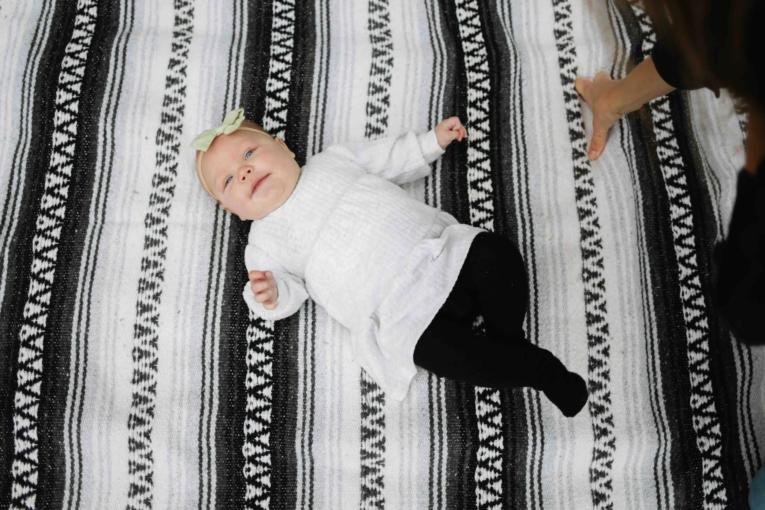 Portrait of newborn Vancouver baby with bow on head lays on outdoorsy blanket