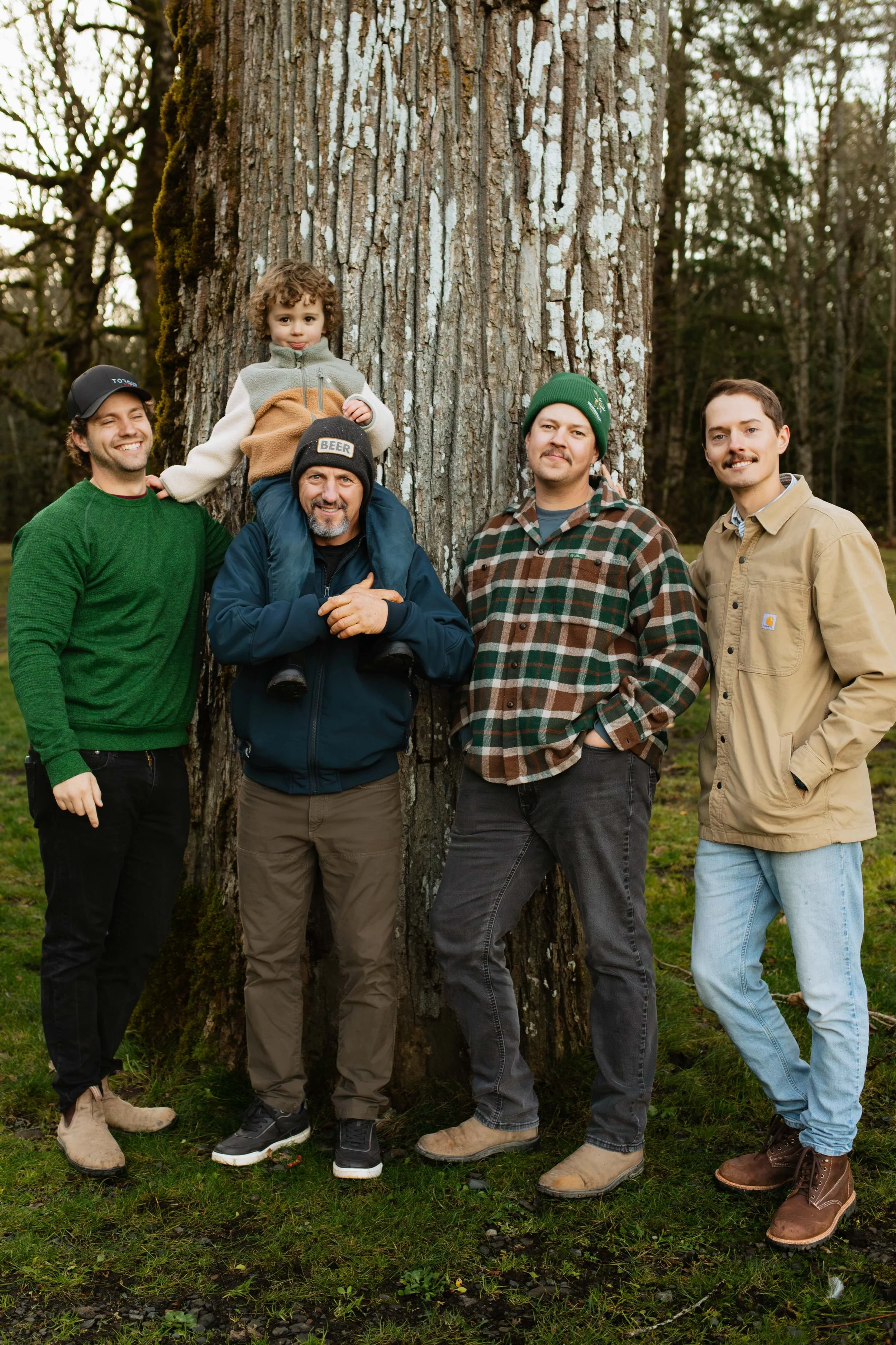 Outdoorsy extended family smiling by tree at Cultus Lake