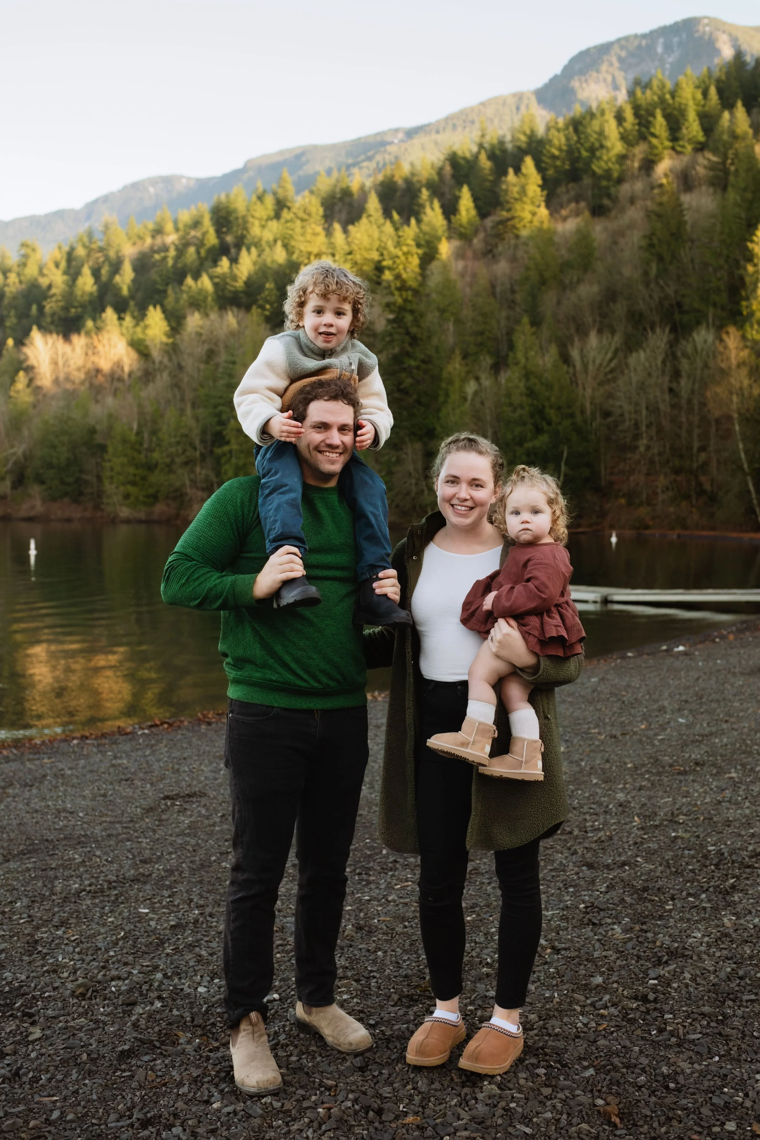 Young Vancouver family smiling at camera with stunning mountain lake background.