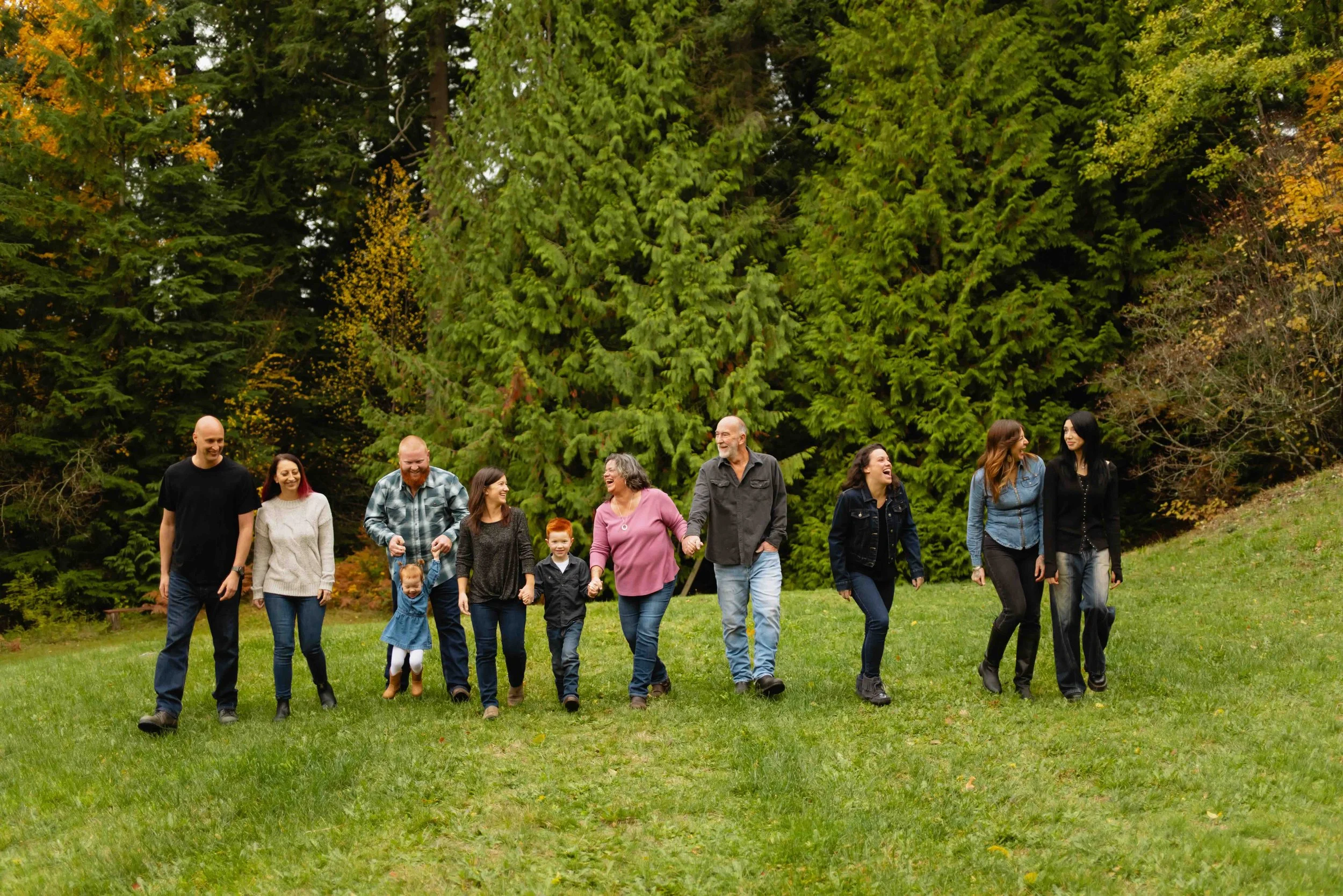 Vancouver extended family walks in line holding hands and laughing forest background