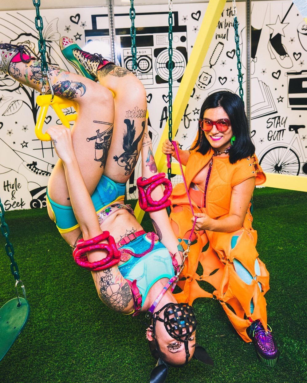 Happy Birthday to @colectivomultipolar , mi amor and fave collaborator! Also happy pride!
[image description: A photo of Sky and Sandra on a swing set with an astroturf floor and a wall with black and white graphic drawings on it. The swing set has y