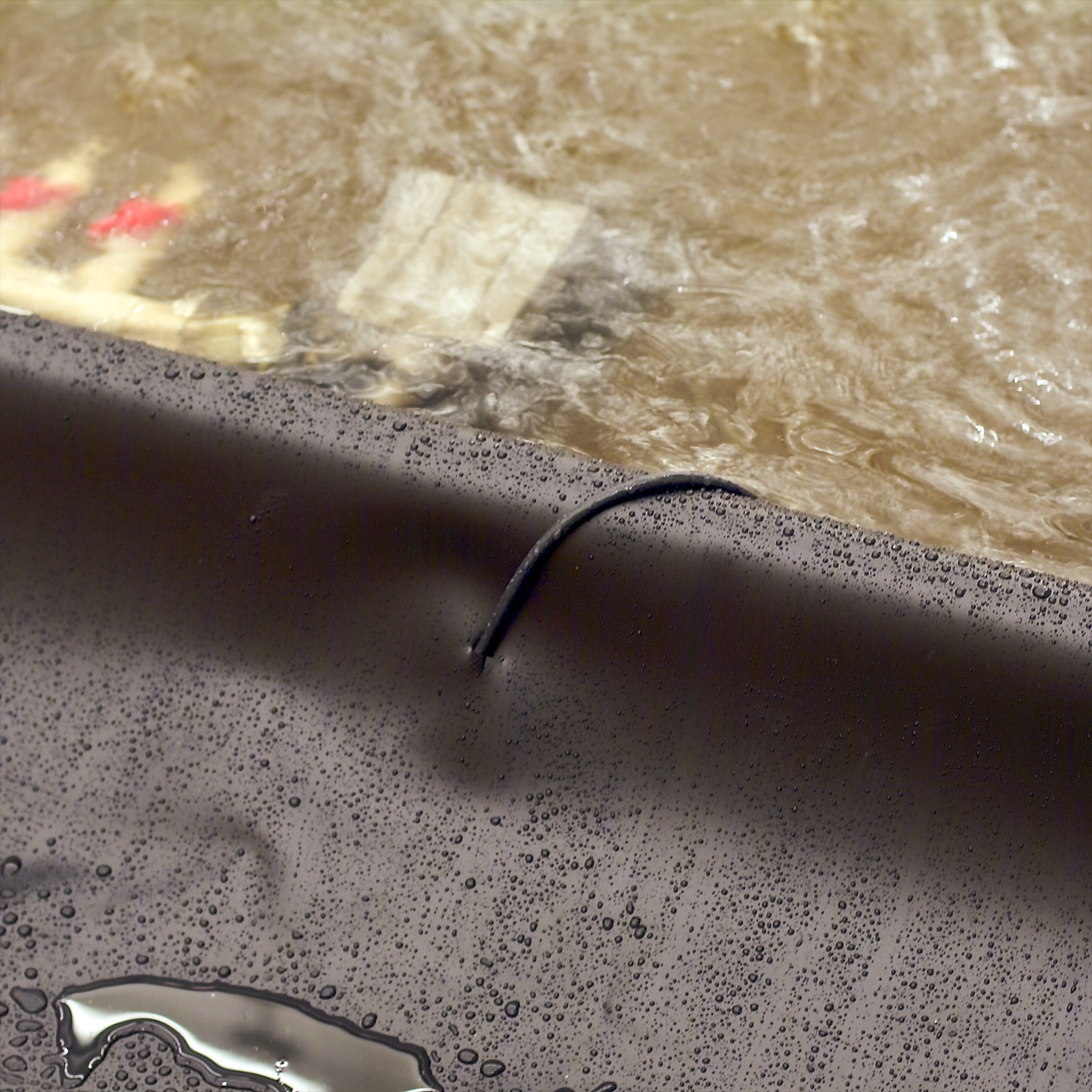 Water flowing over a dark surface with droplets and a black cable protruding through it.