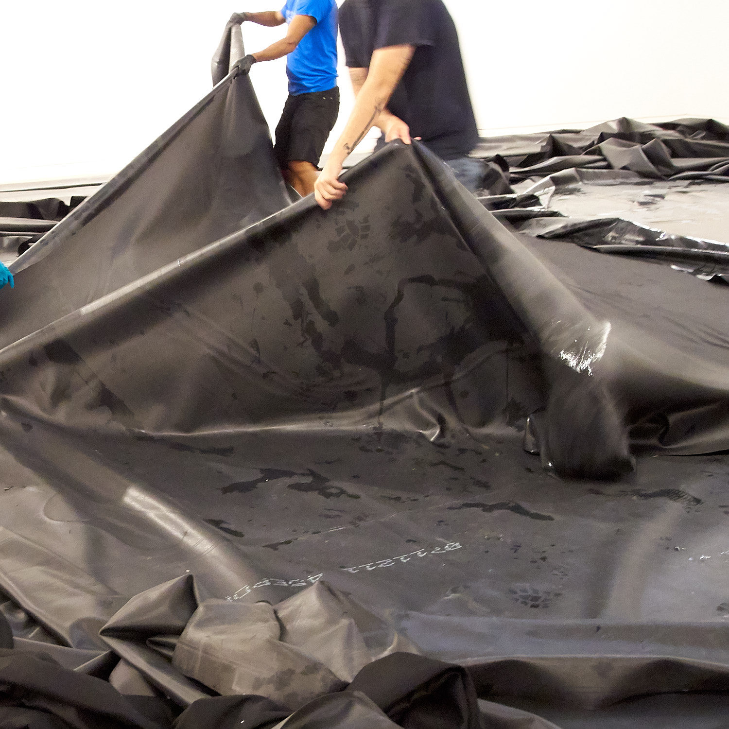 People handling large black plastic sheets indoors.