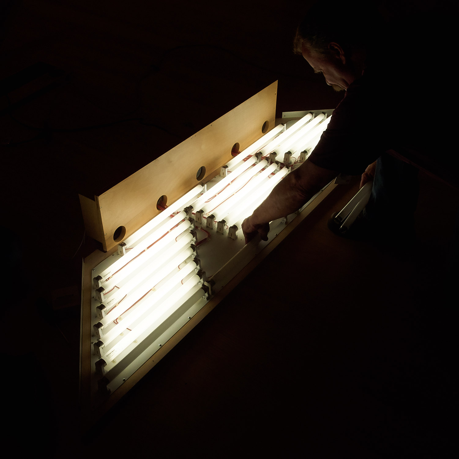 Person assembling or repairing a fluorescent light fixture in a dimly lit area.