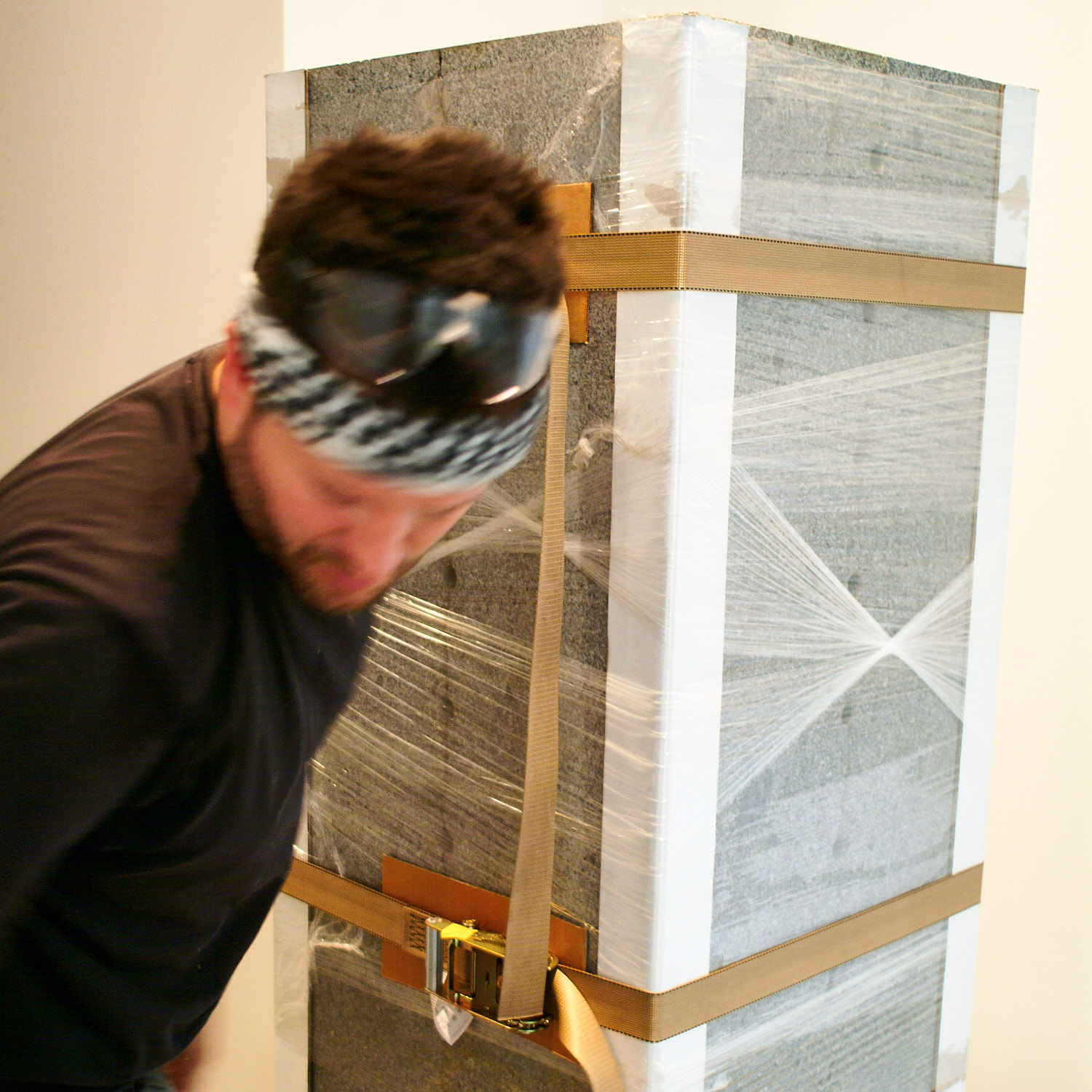 Man with headband securing gray structure with straps and plastic wrap.