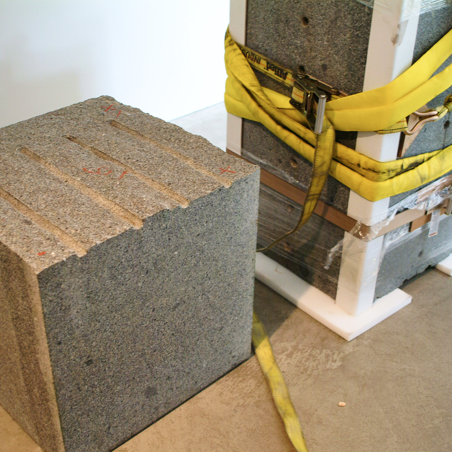 Large gray stone blocks partially wrapped with yellow straps and packing materials placed on a concrete floor.