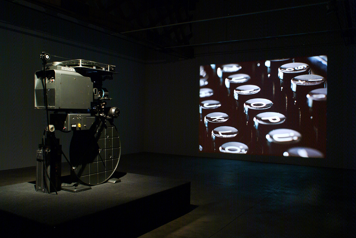 Film projector displaying vintage typewriter keys on a screen in a dimly lit room.